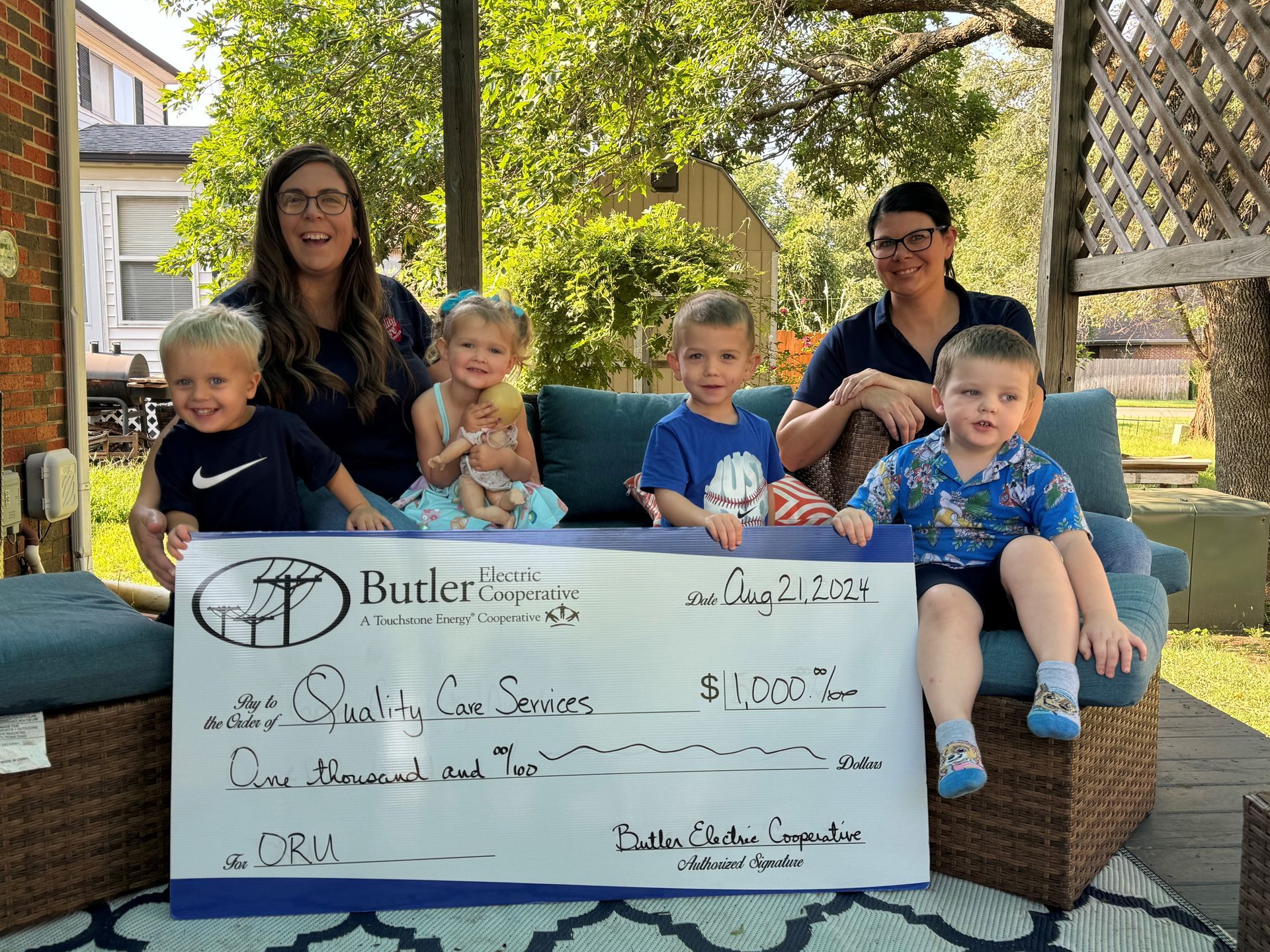 A group of children are sitting on a couch holding a check.