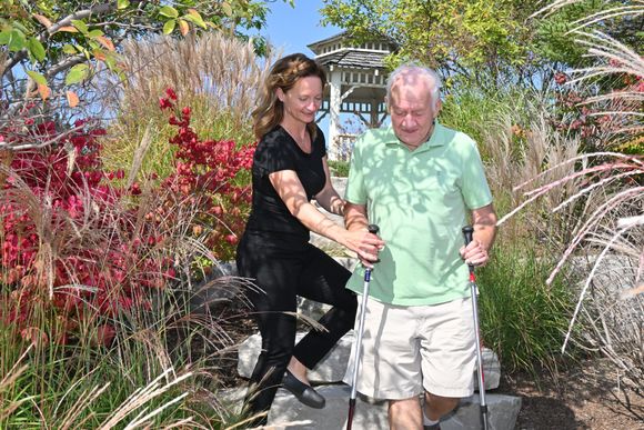 Physiotherapist helping client walk down a flight of stairs on a path in the park surrounded by lush foliage.