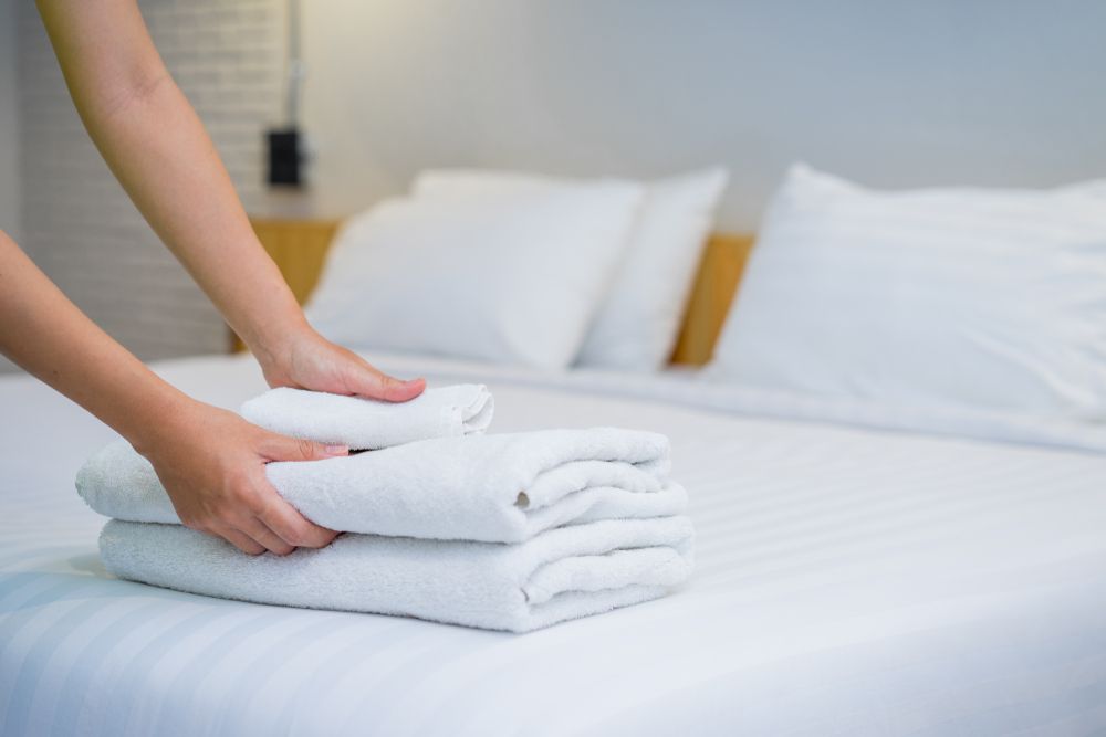 A person is stacking towels on top of each other on a bed. — Tuncurry Washerteria In Nabiac, NSW