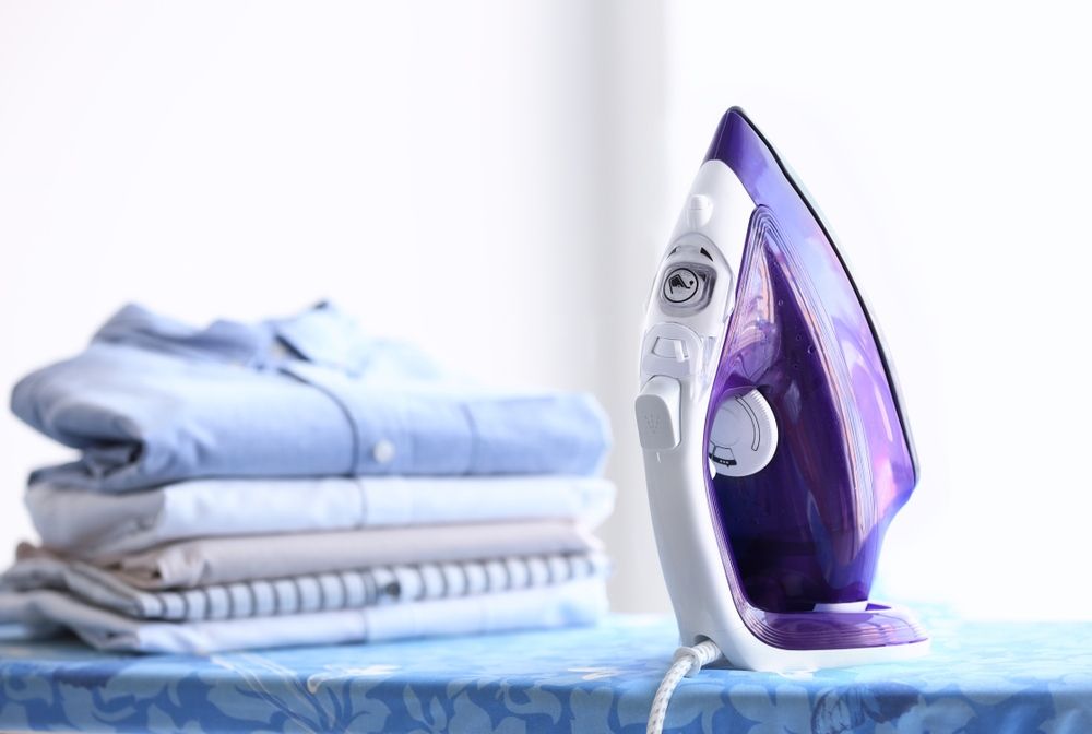 A Purple Iron is Sitting on an Ironing Board Next to a Pile of Clothes — Tuncurry Washerteria In Tuncurry, NSW
