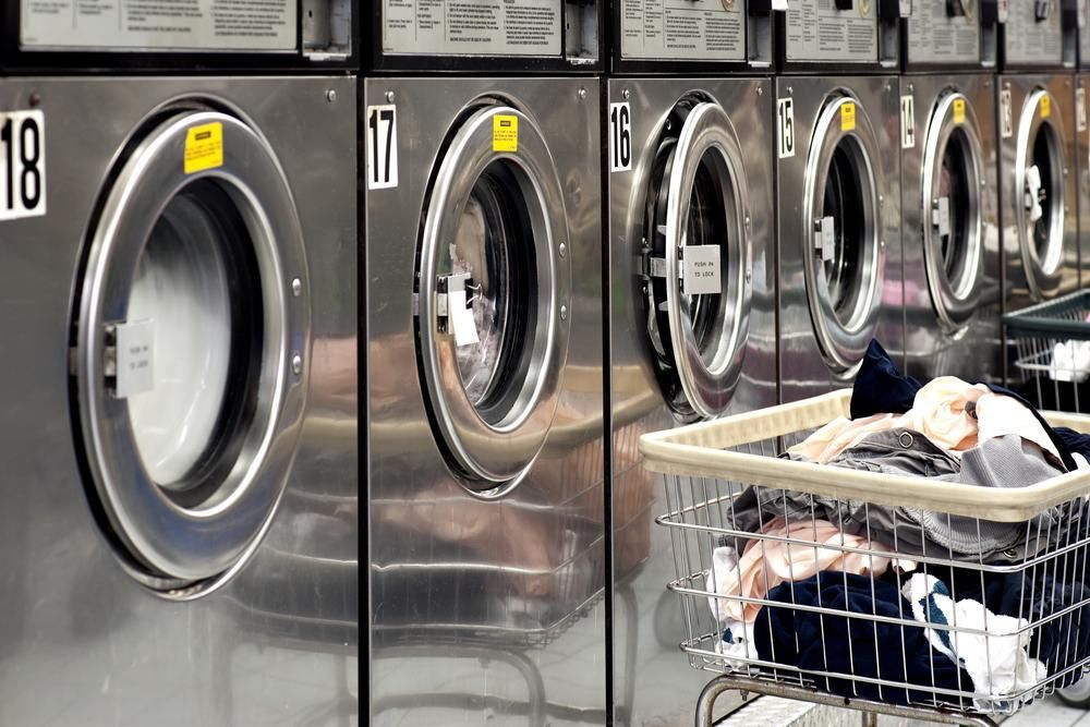 A row of washing machines in a laundromat with a basket full of clothes. — Tuncurry Washerteria In Nabiac, NSW