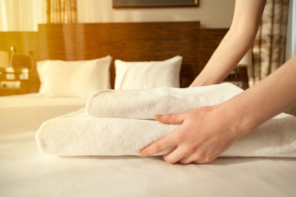 A Woman is Stacking Towels on a Bed in a Hotel Room — Tuncurry Washerteria In Nabiac, NSW