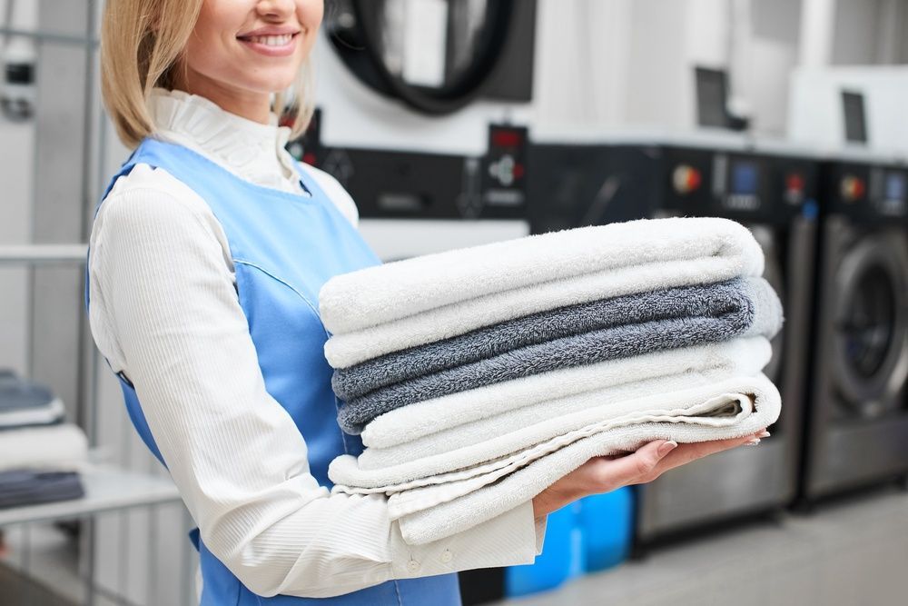 A Woman is Holding a Stack of Towels in a Laundromat — Tuncurry Washerteria In Pacific Palms, NSW