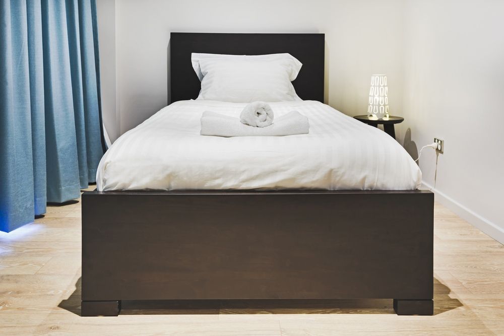 A Single Bed With White Sheets and Pillows in a Hotel Room — Tuncurry Washerteria In Pacific Palms, NSW