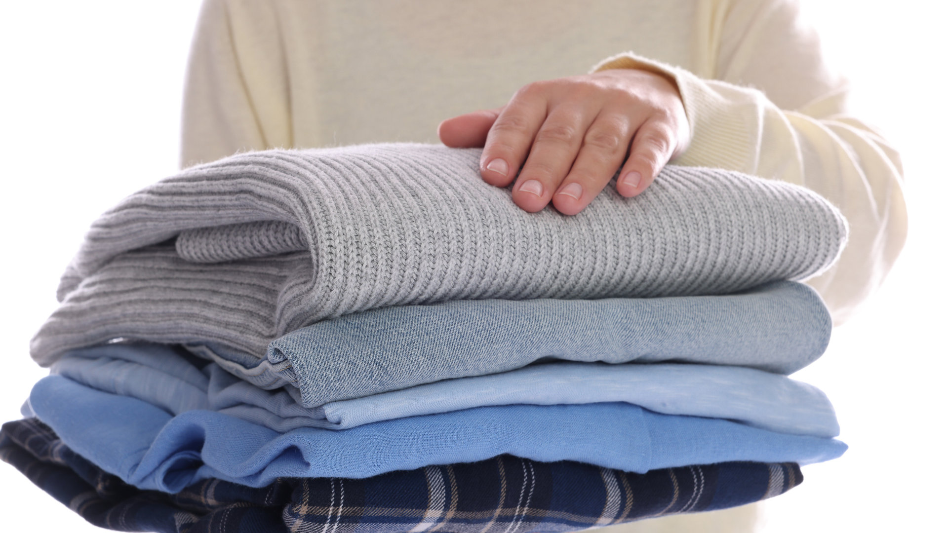 A white plastic laundry basket filled with clothes stands in a laundromat next to a row of commercial dryers.