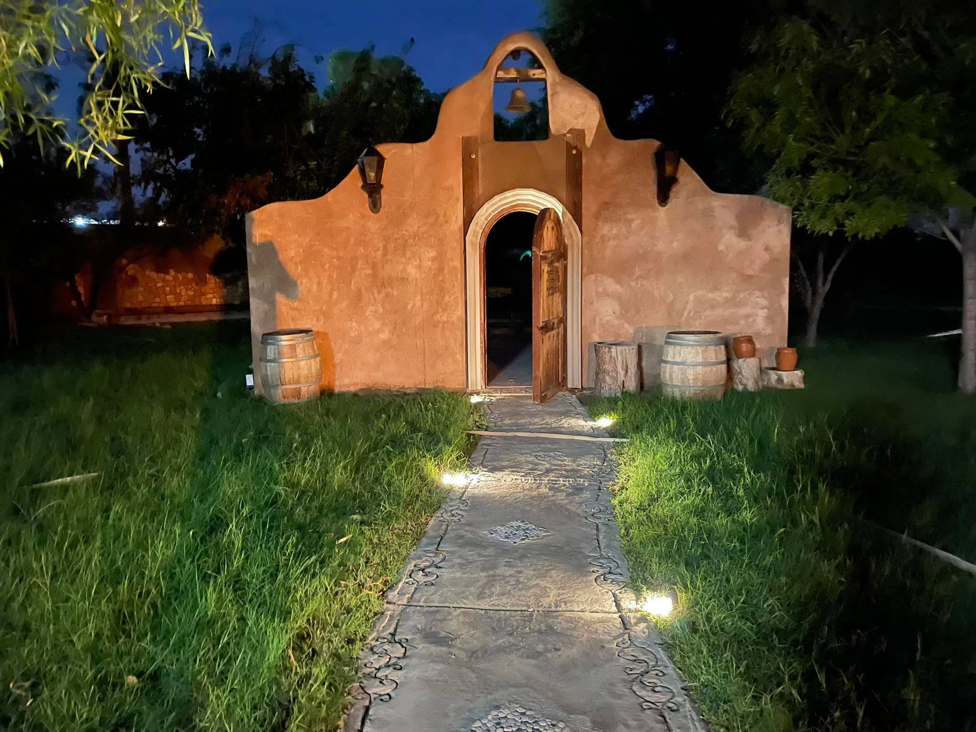 A stone walkway leading to a building with barrels in front of it at night.