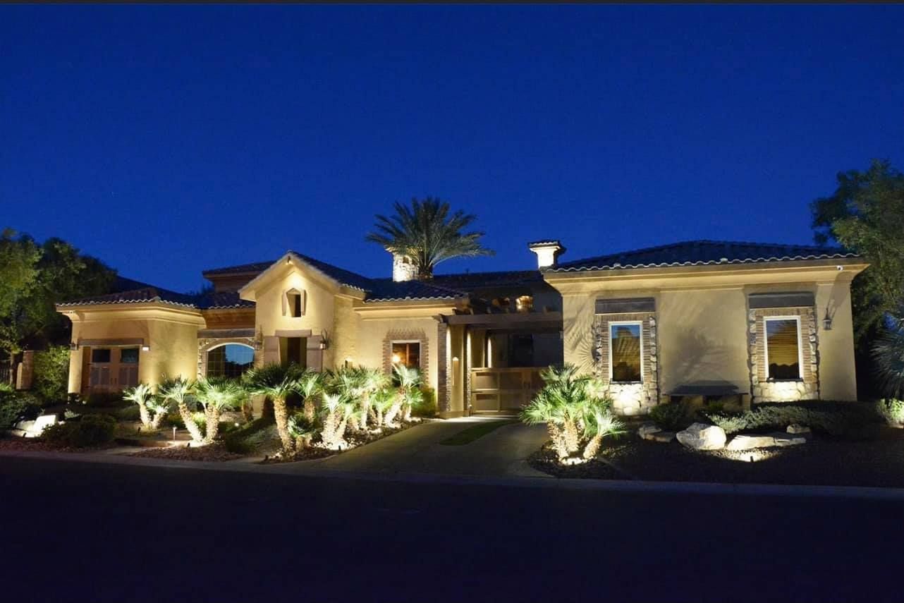 A large house is lit up at night with palm trees in front of it
