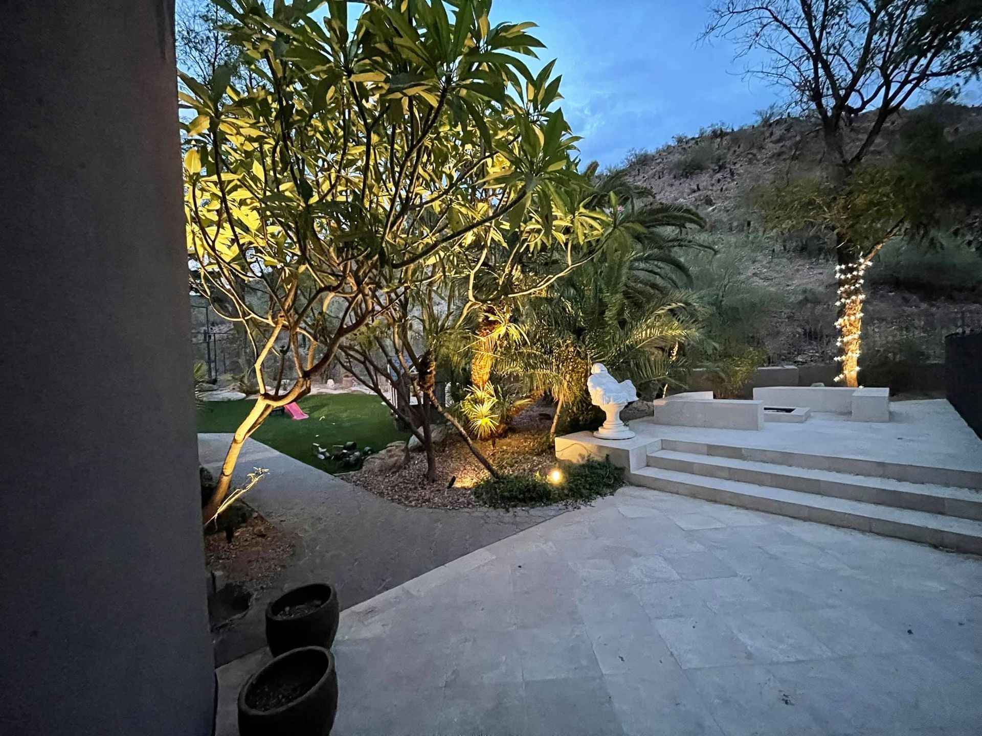 A patio with stairs leading up to a lush green hillside at night.
