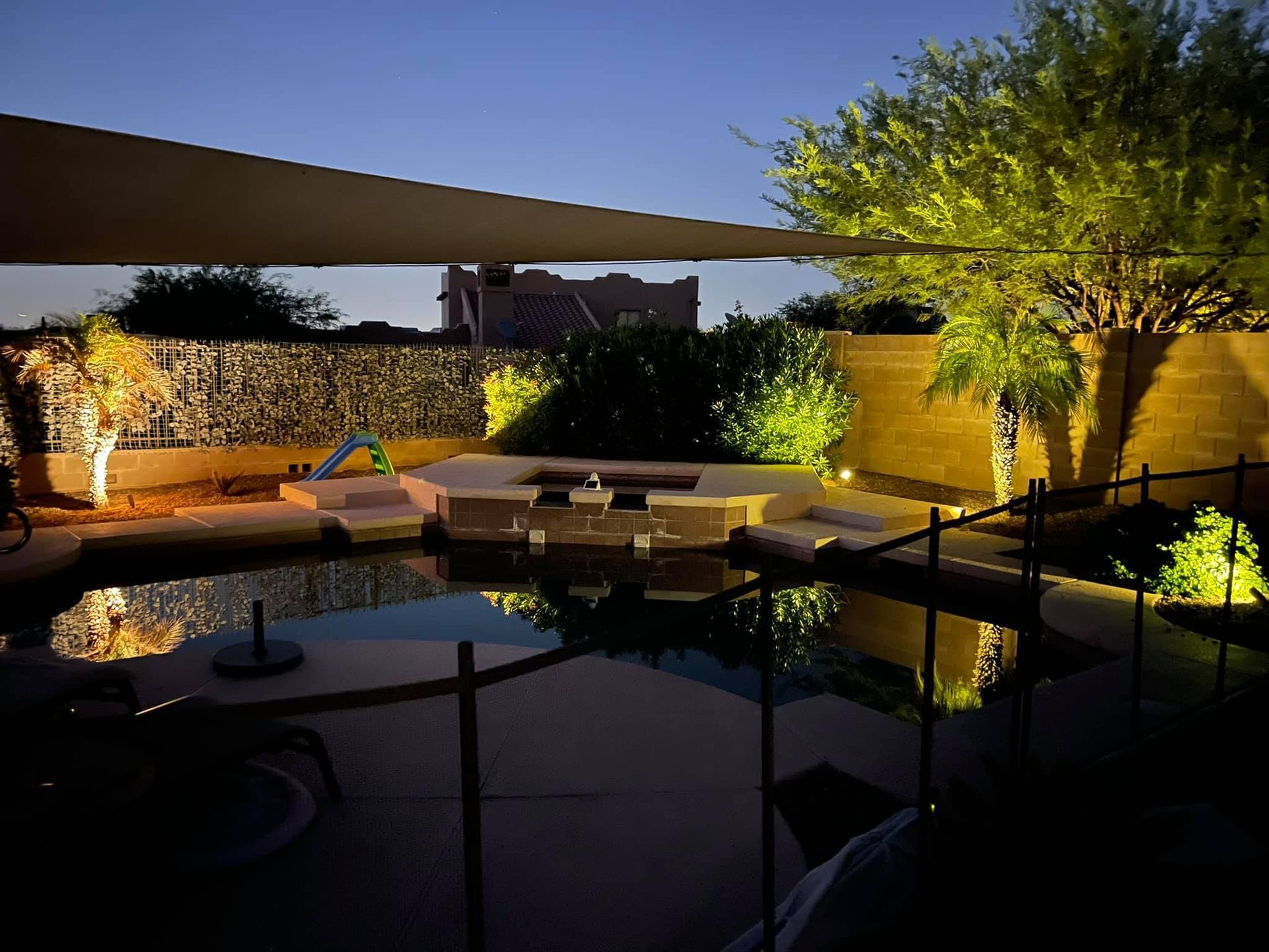 A backyard with a fence and a swimming pool at night