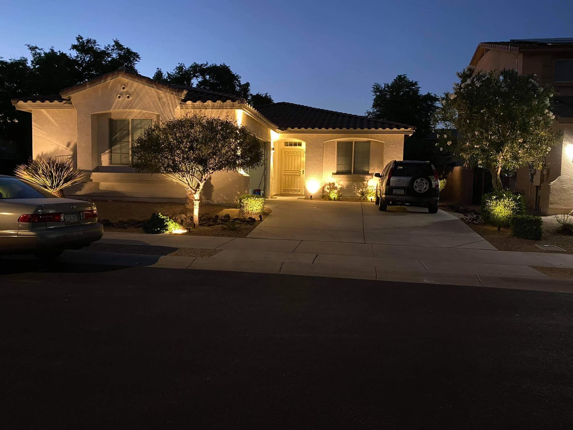 A car is parked in front of a house that is lit up at night.