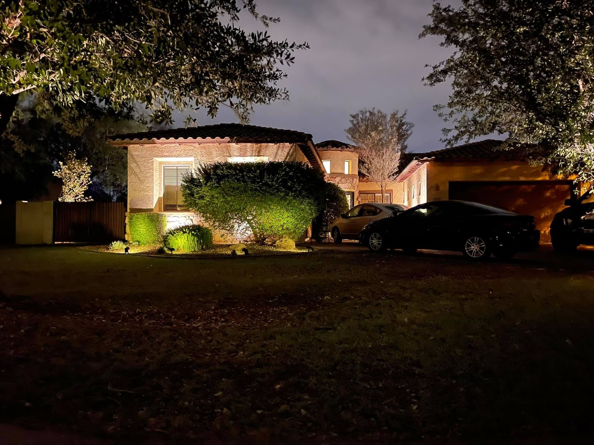 A house is lit up at night with cars parked in front of it