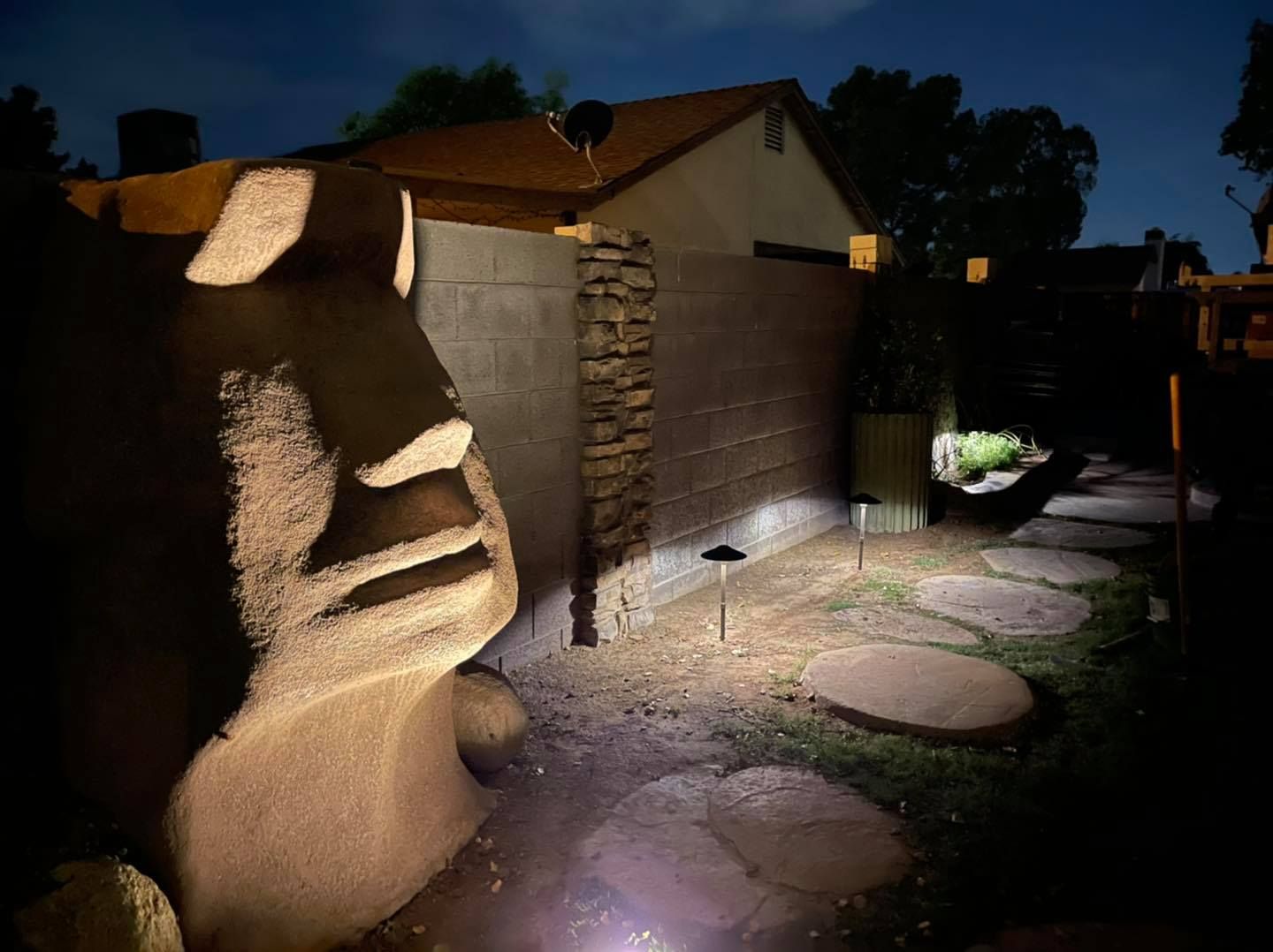 A statue of a face is lit up in a backyard at night.