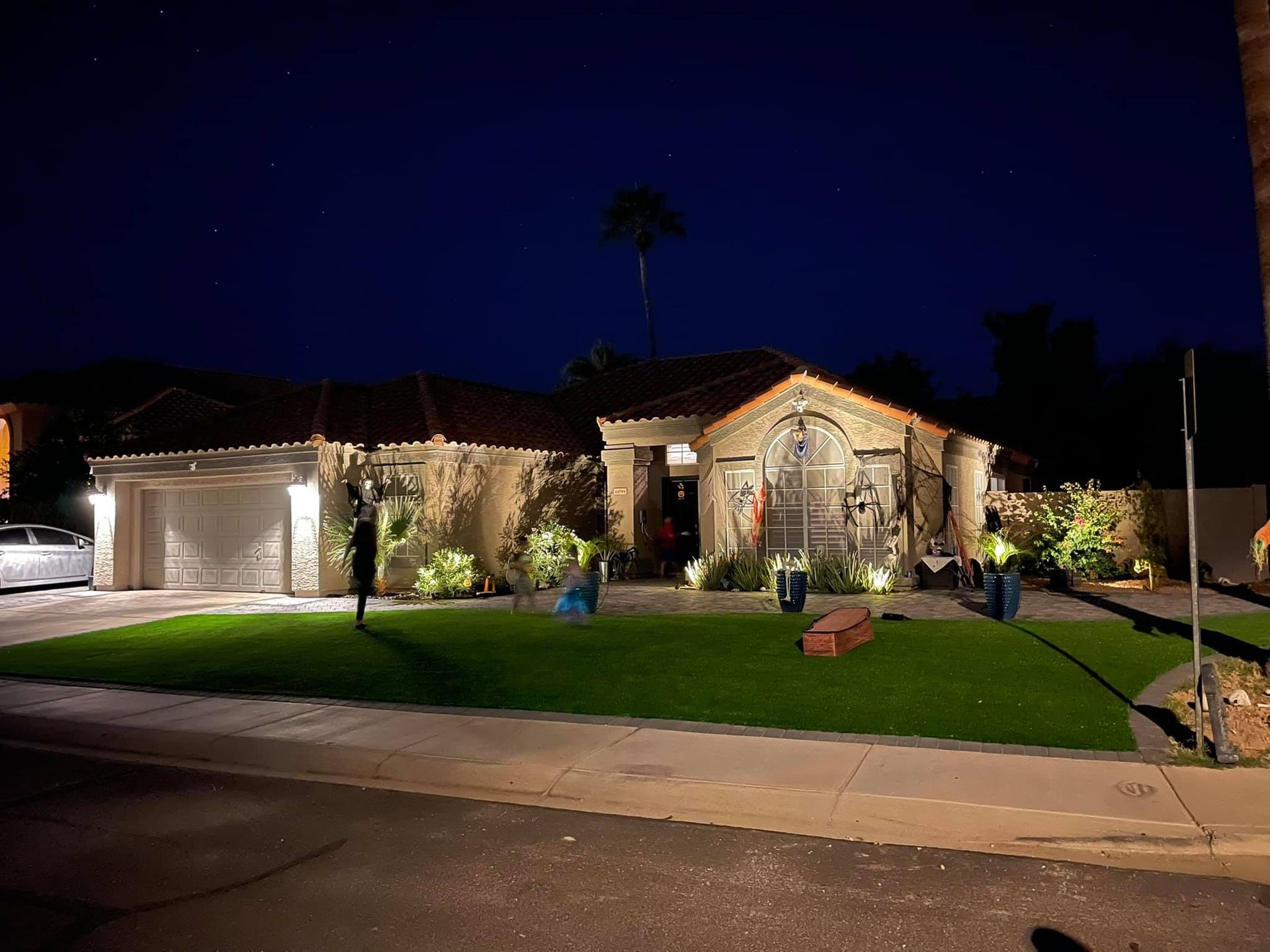 A house is lit up at night with a car parked in front of it.