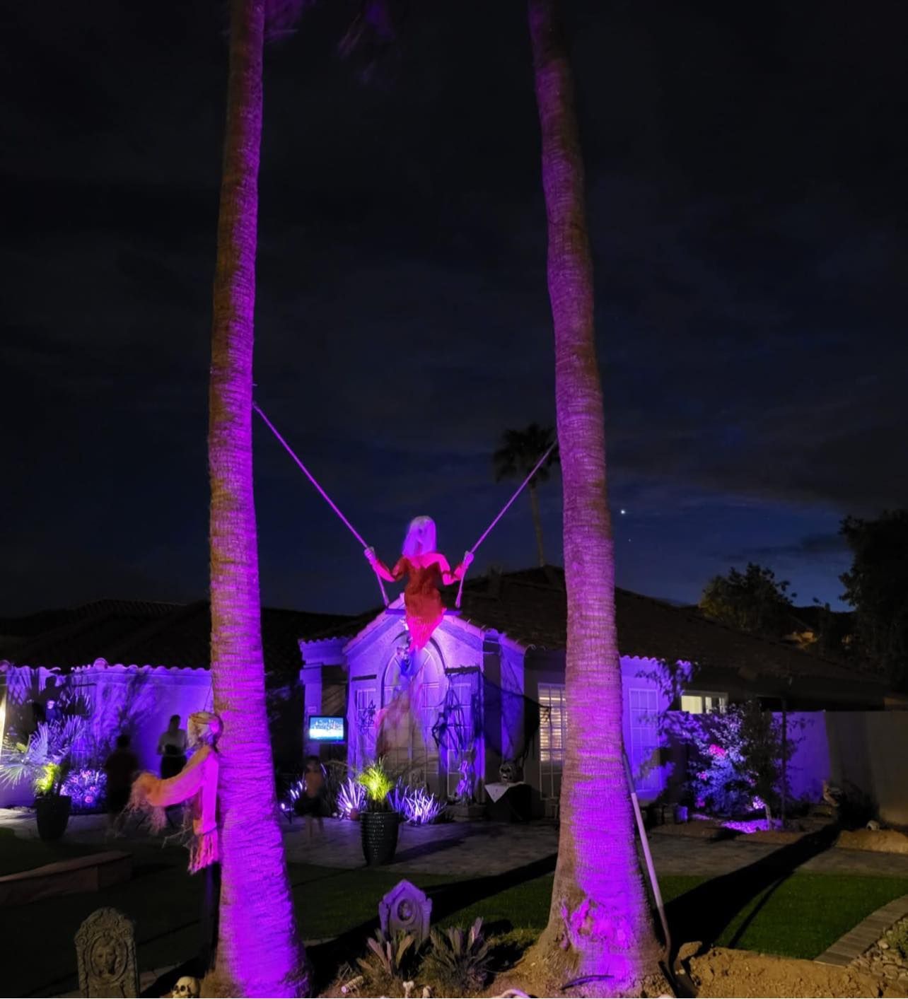 A statue of a woman on a swing is lit up with purple lights.
