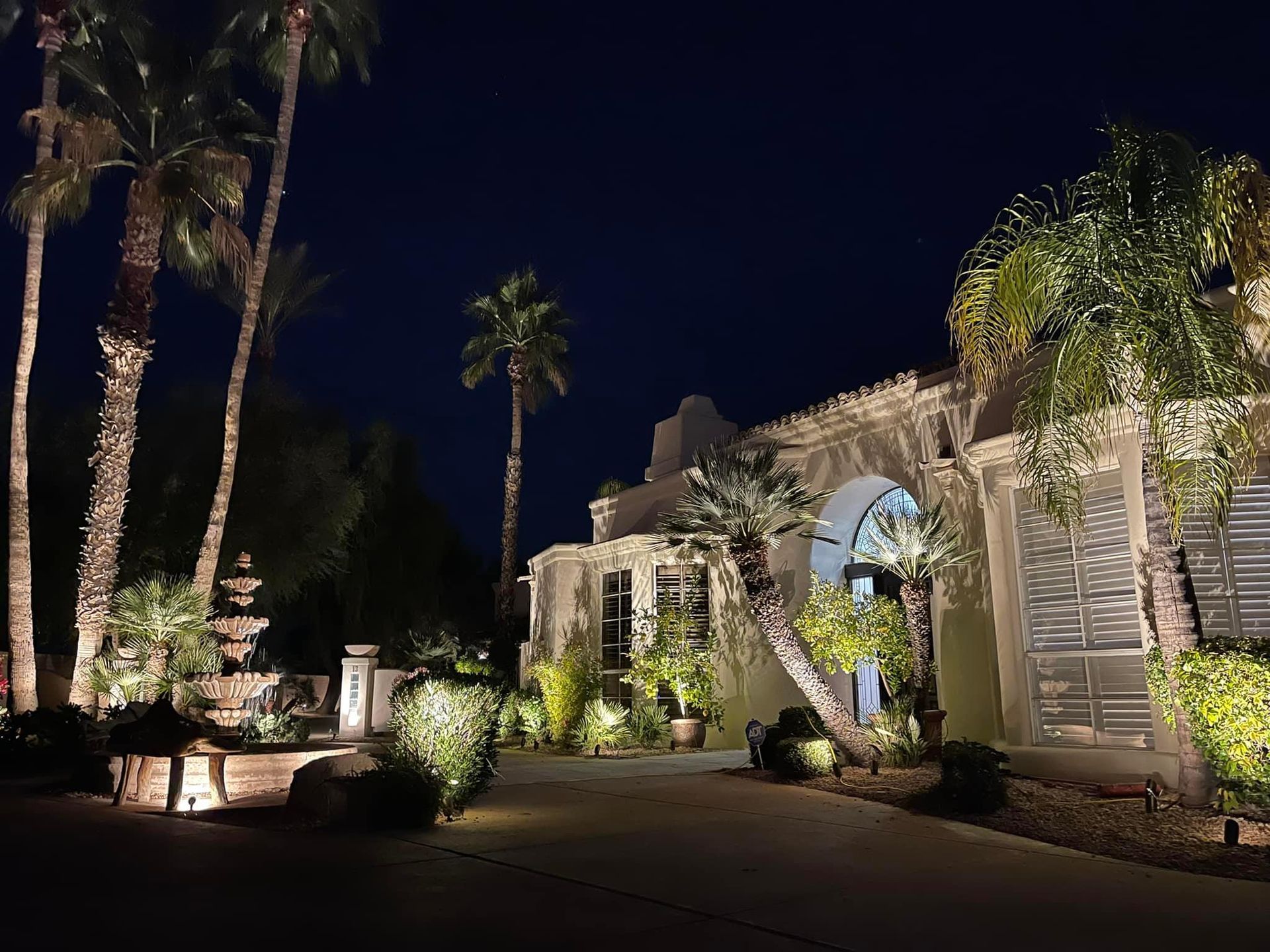 A large house is lit up at night with palm trees in front of it