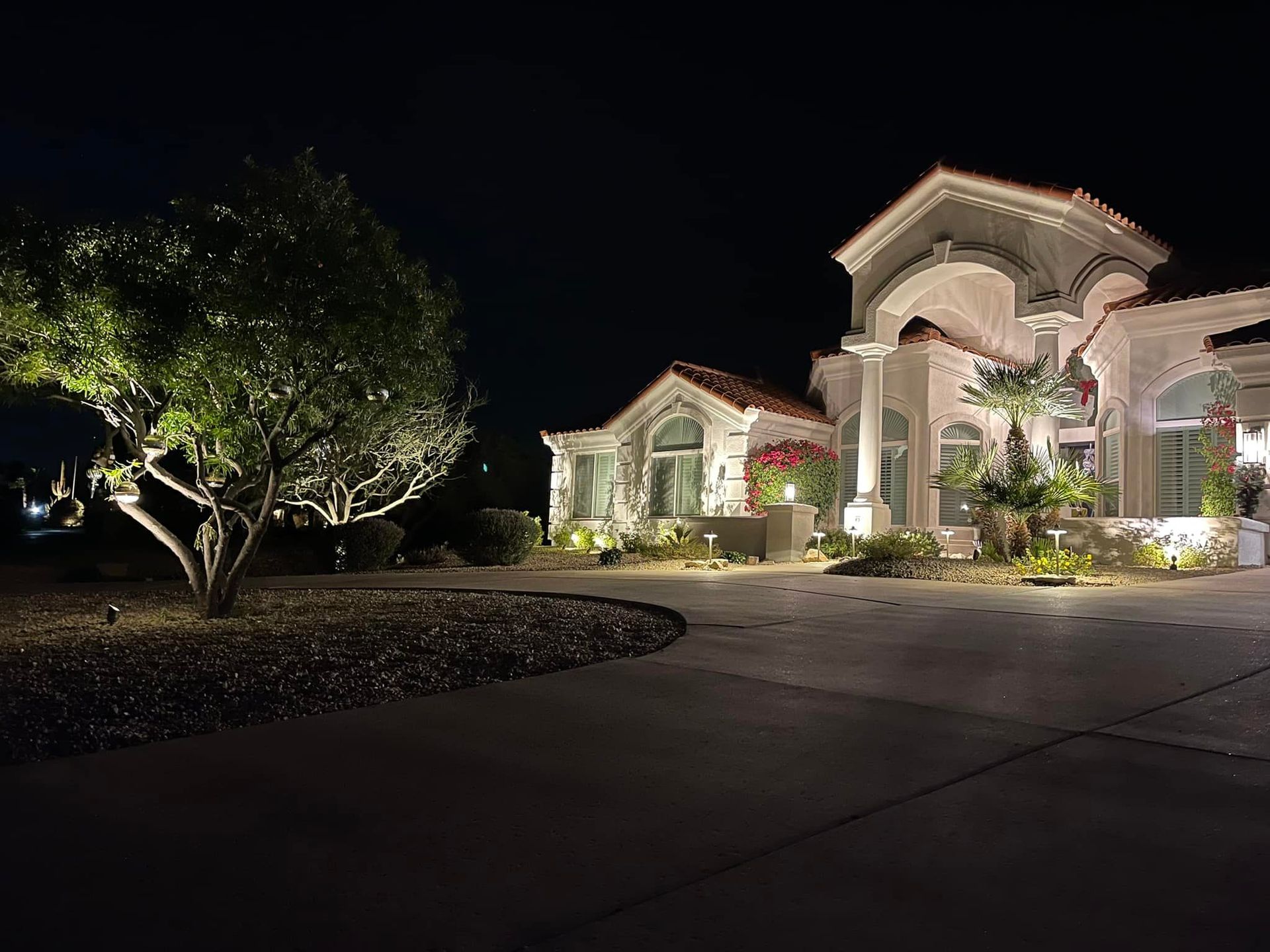 A large house is lit up at night with trees in front of it.
