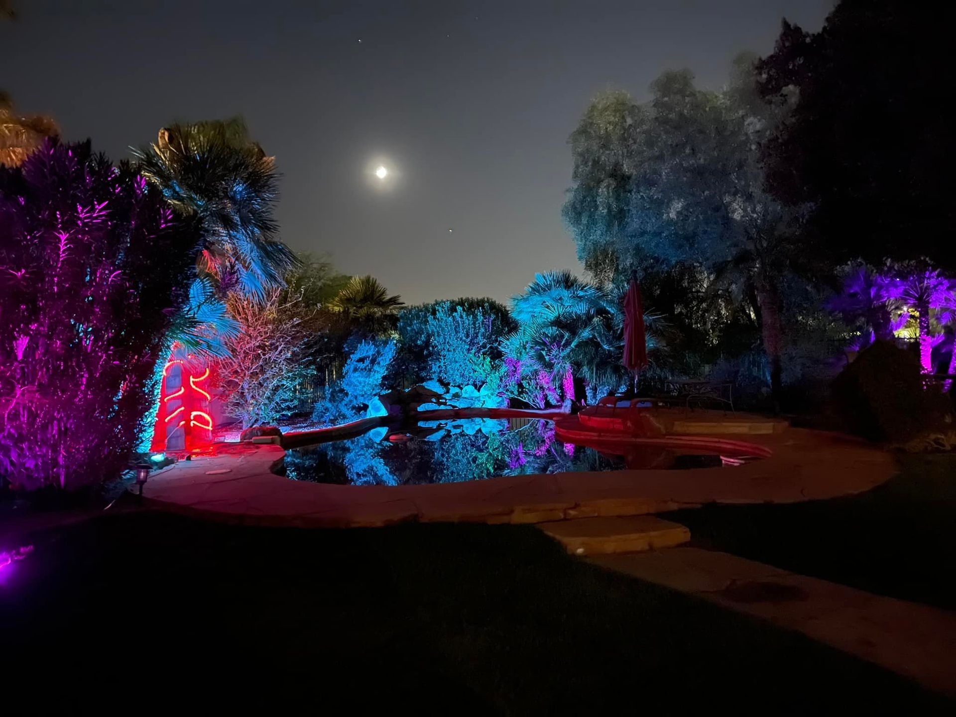 A swimming pool is lit up with purple and blue lights at night.