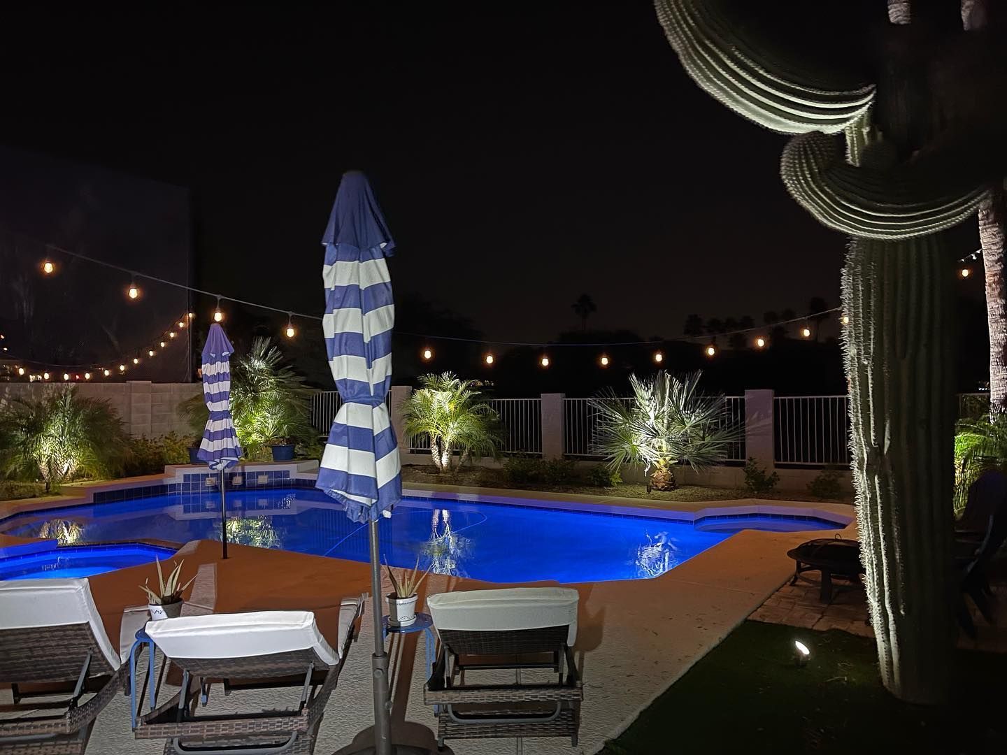 A large swimming pool is lit up at night with umbrellas and chairs around it.
