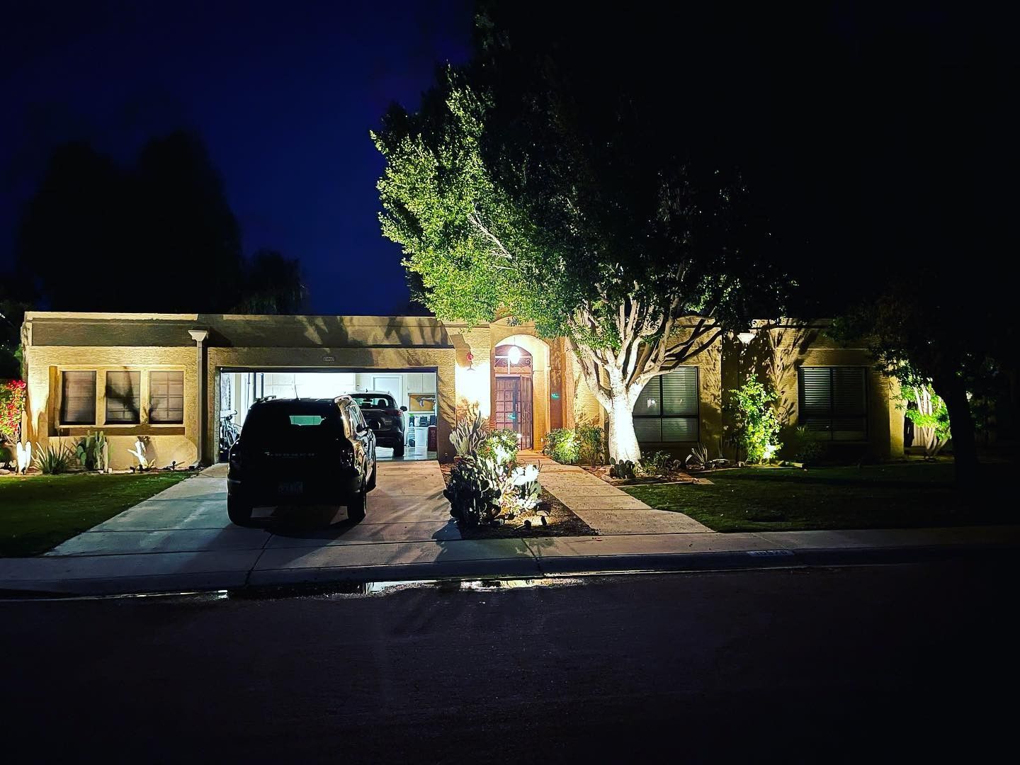 A house is lit up at night with a car parked in front of it.