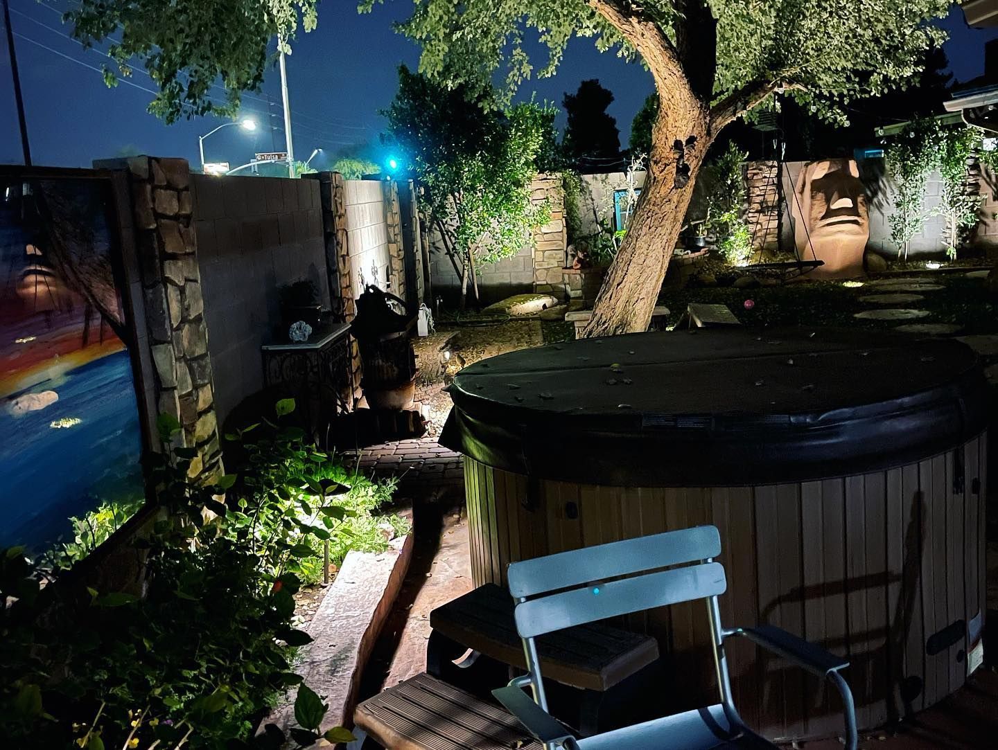 A wooden hot tub is sitting under a tree in a backyard at night.