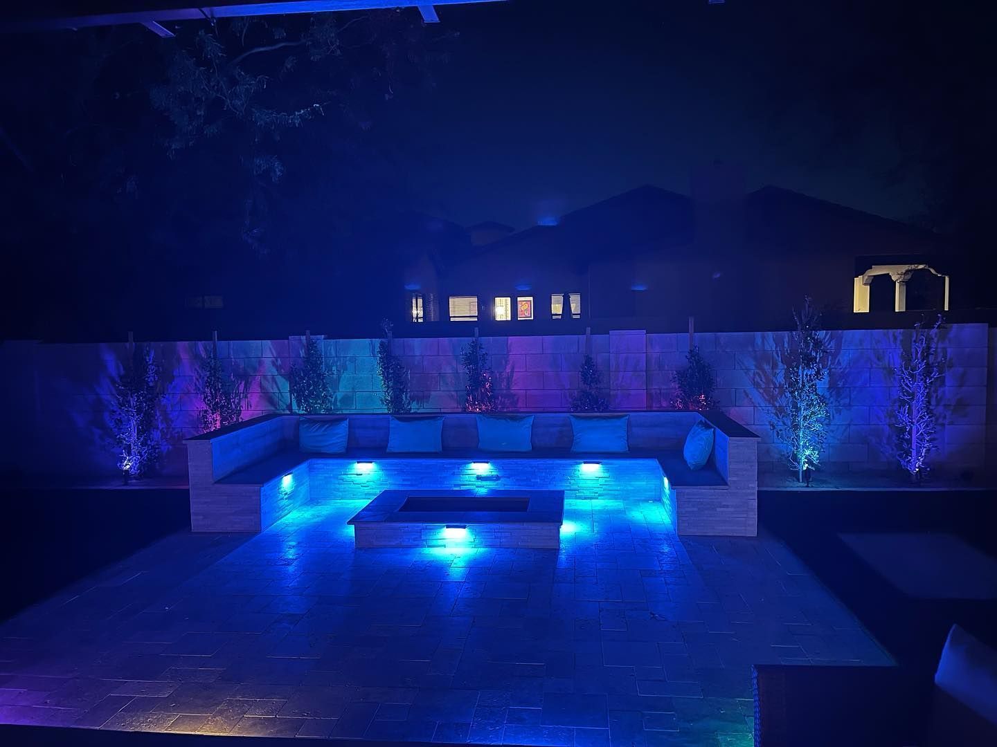 A patio with a fire pit and a couch lit up at night.