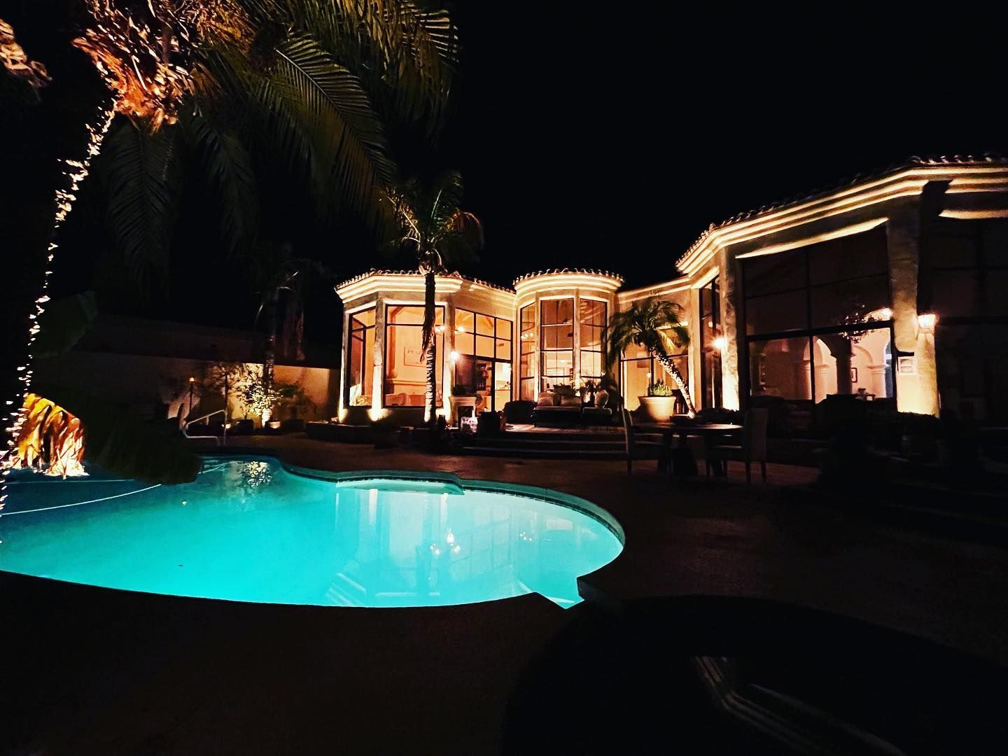 A large house with a swimming pool in front of it at night.