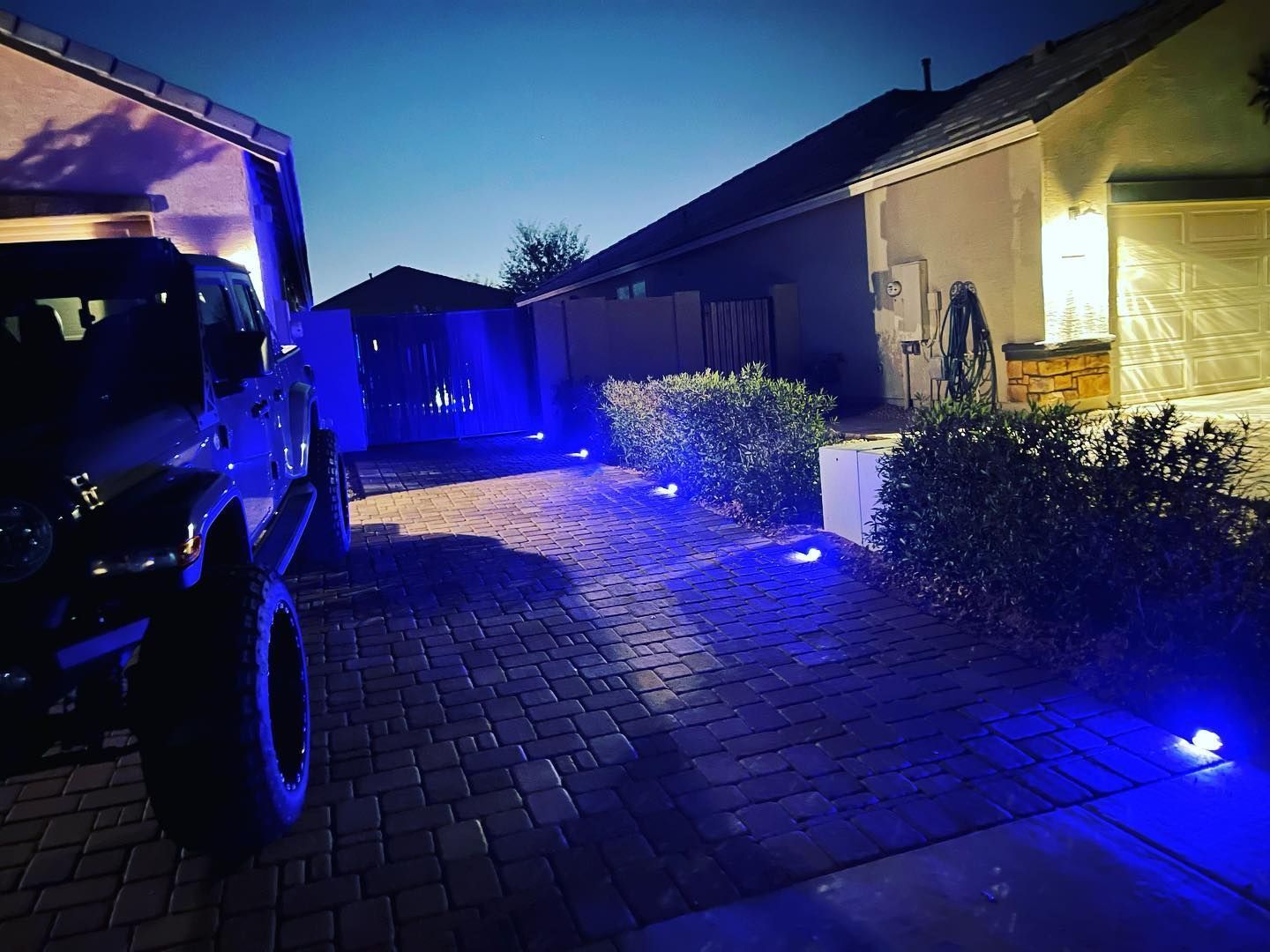 A truck is parked in front of a house with blue lights on the ground.