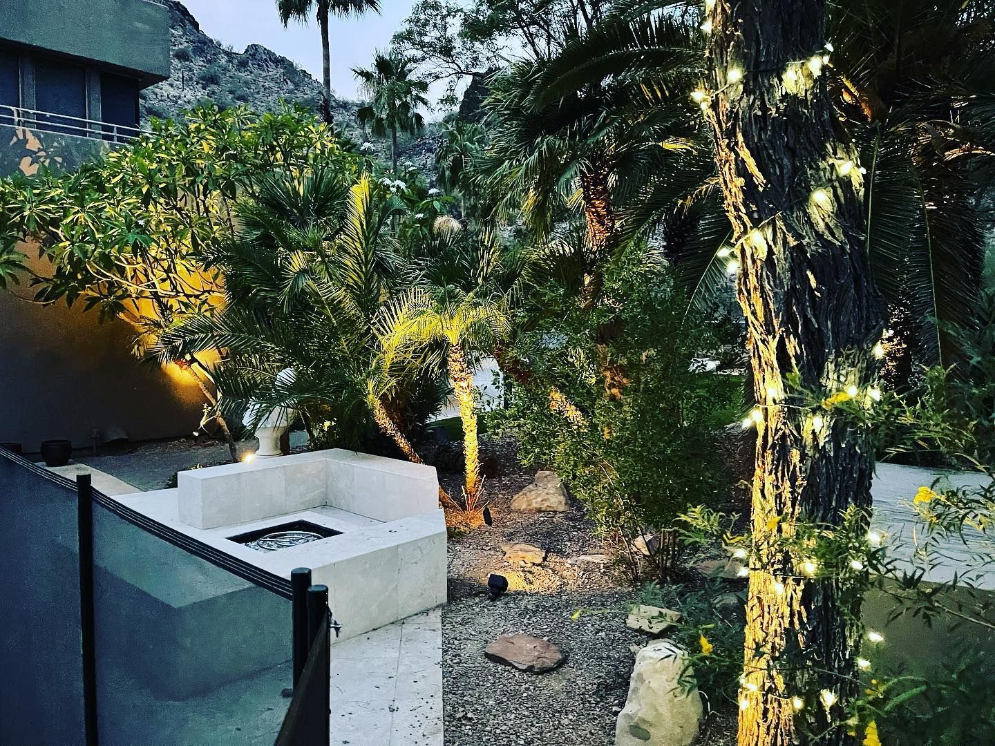 A patio with a fire pit and a tree with lights on it.