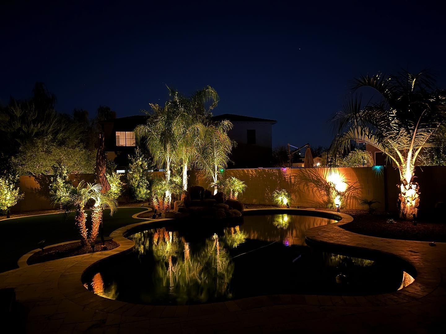 A swimming pool is lit up at night in a backyard.