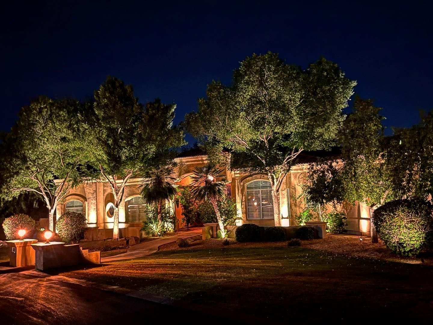 A house is lit up at night with trees in front of it.