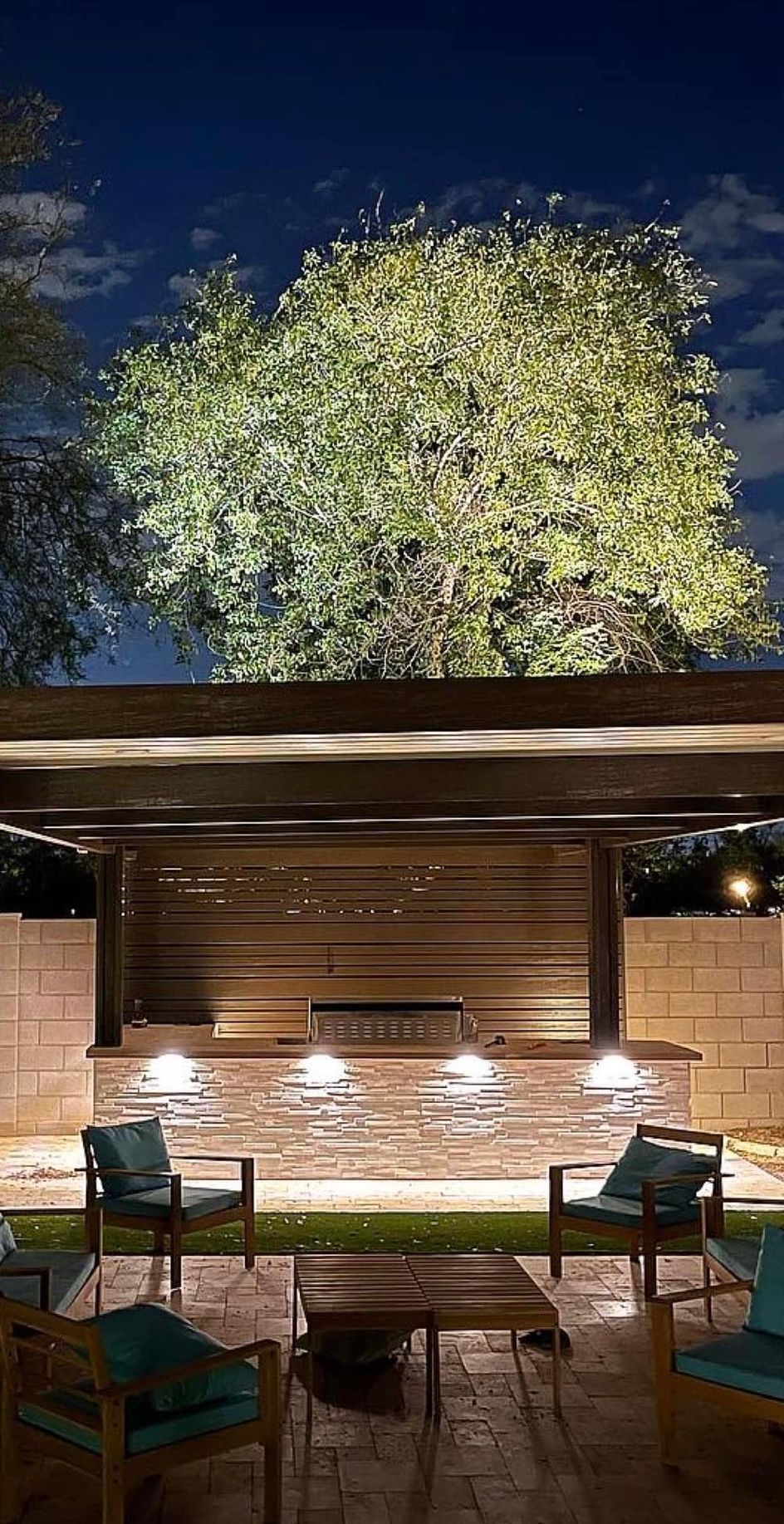 A patio with chairs , a table and a tree at night.