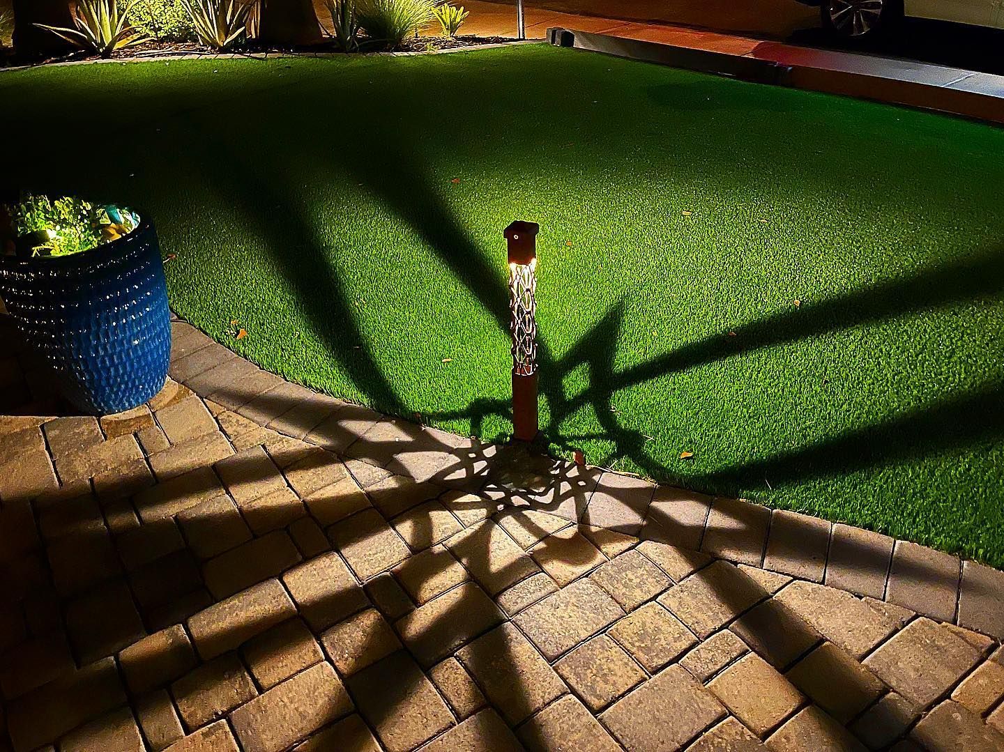 A shadow of a tree is cast on a brick walkway next to a lawn.