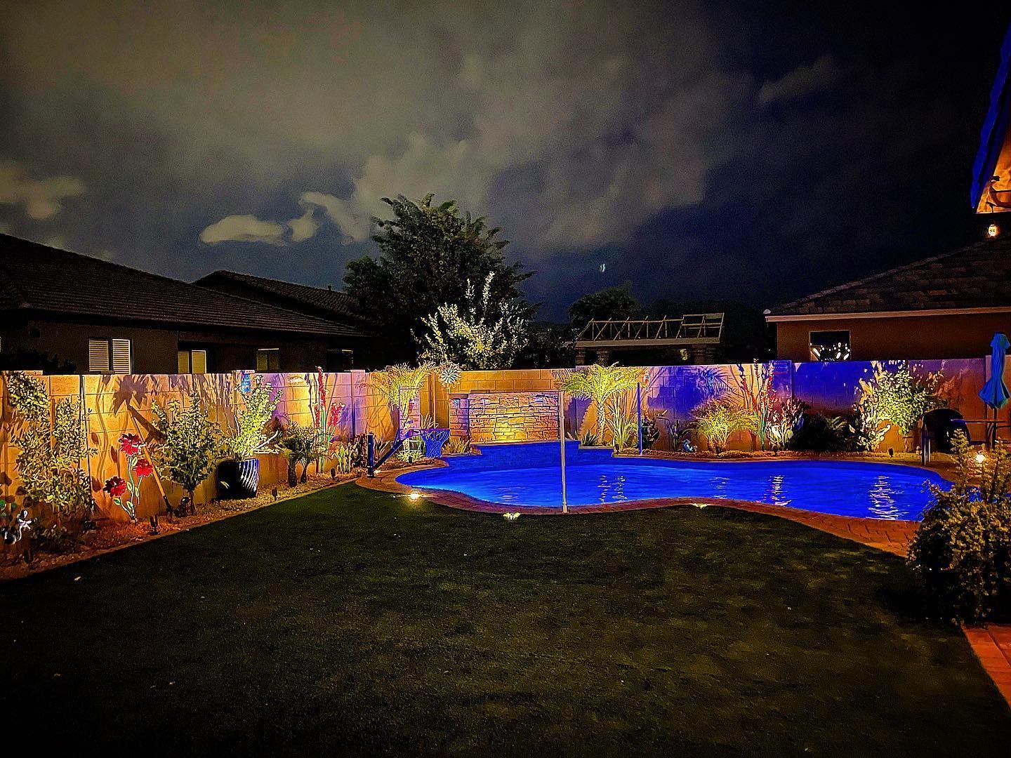 A large swimming pool is lit up at night in a backyard