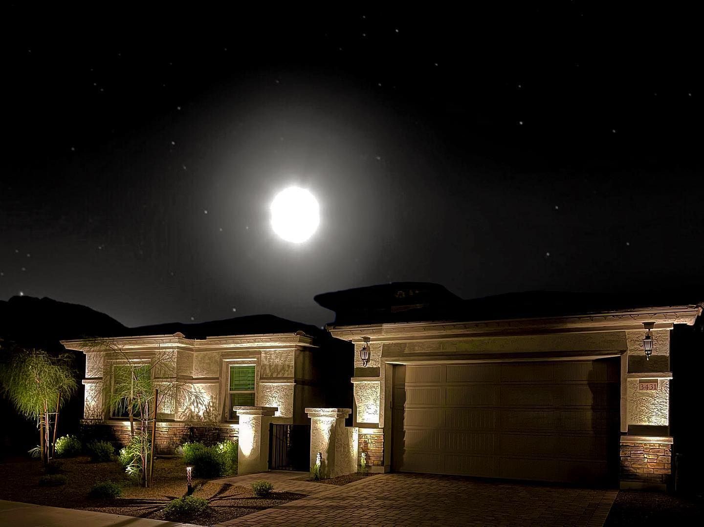 A house is lit up at night with a full moon in the sky.
