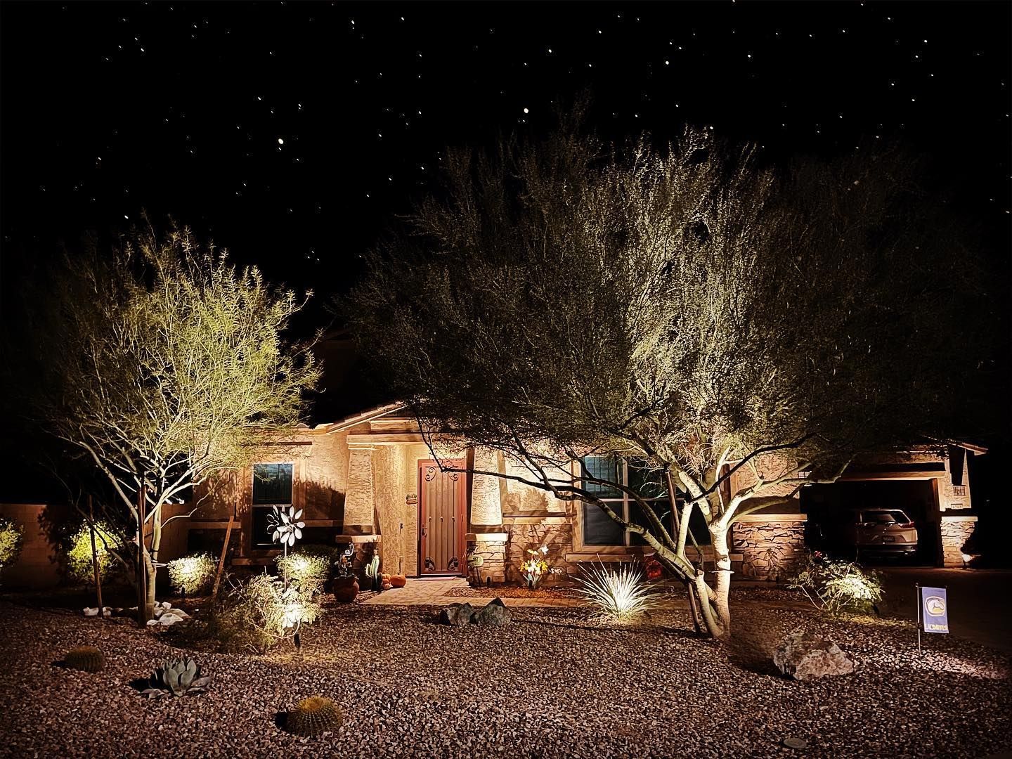 A house is lit up at night with trees in front of it.