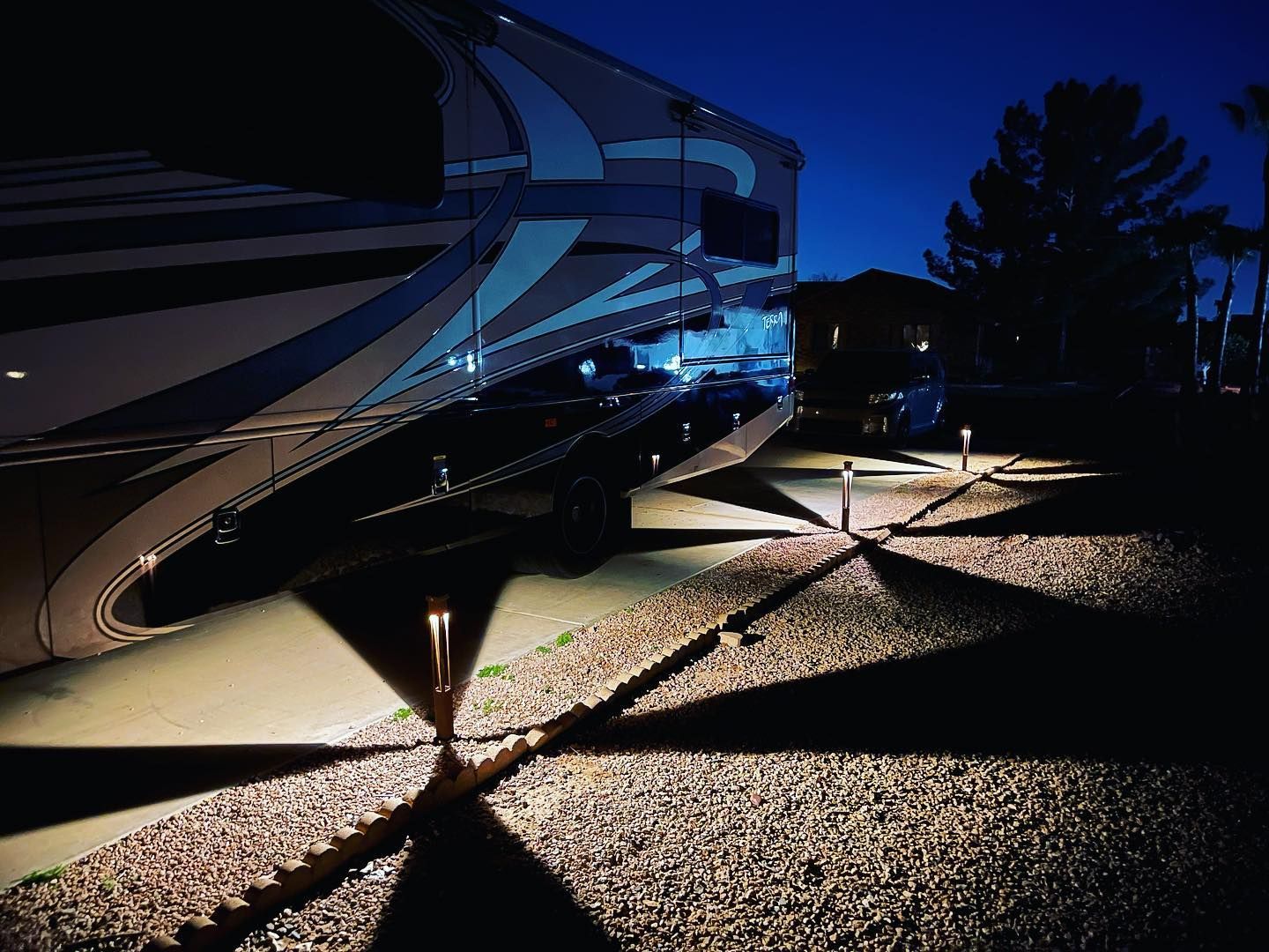 A rv is parked in a gravel driveway at night
