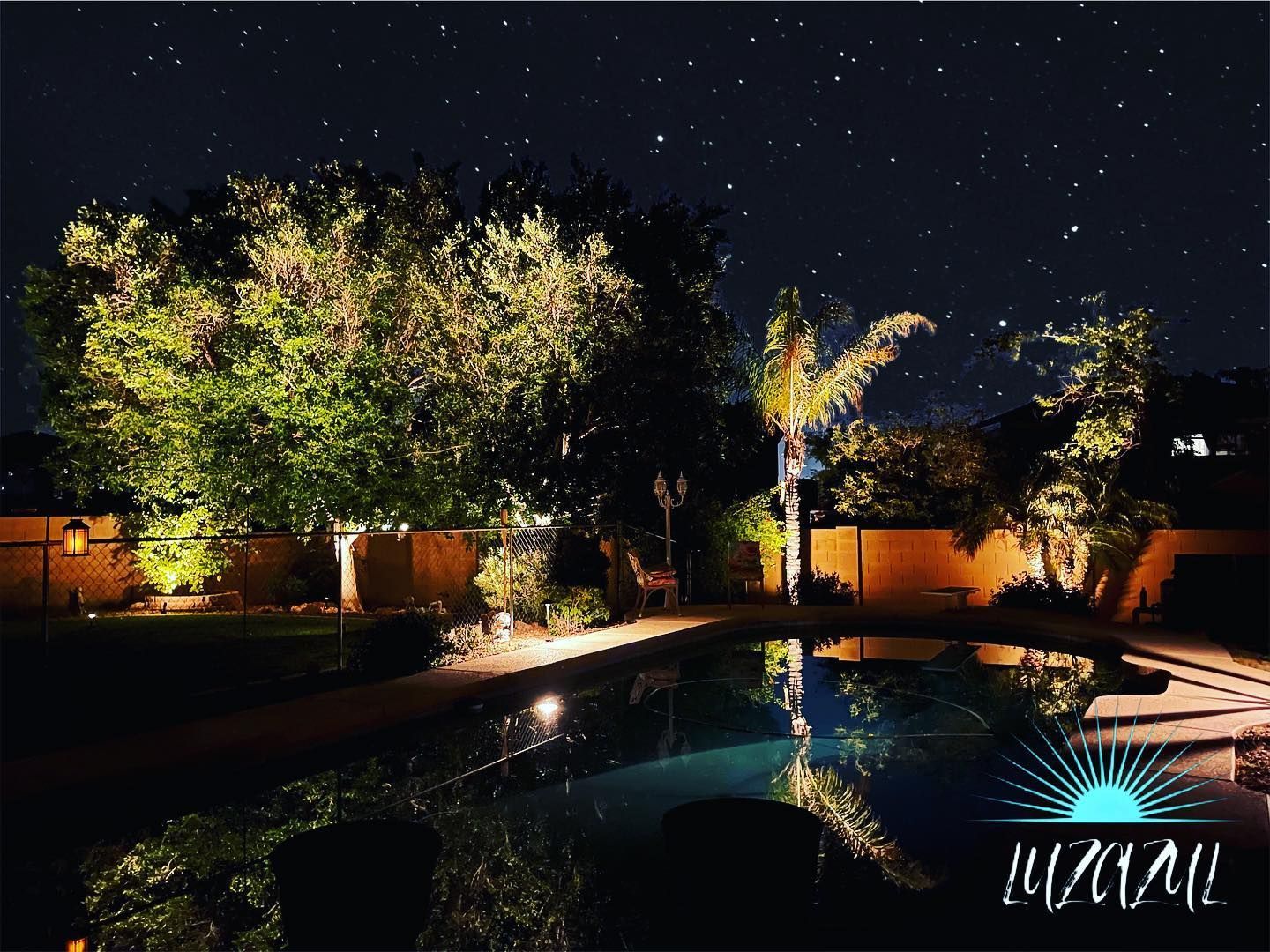 A swimming pool is lit up at night in a backyard