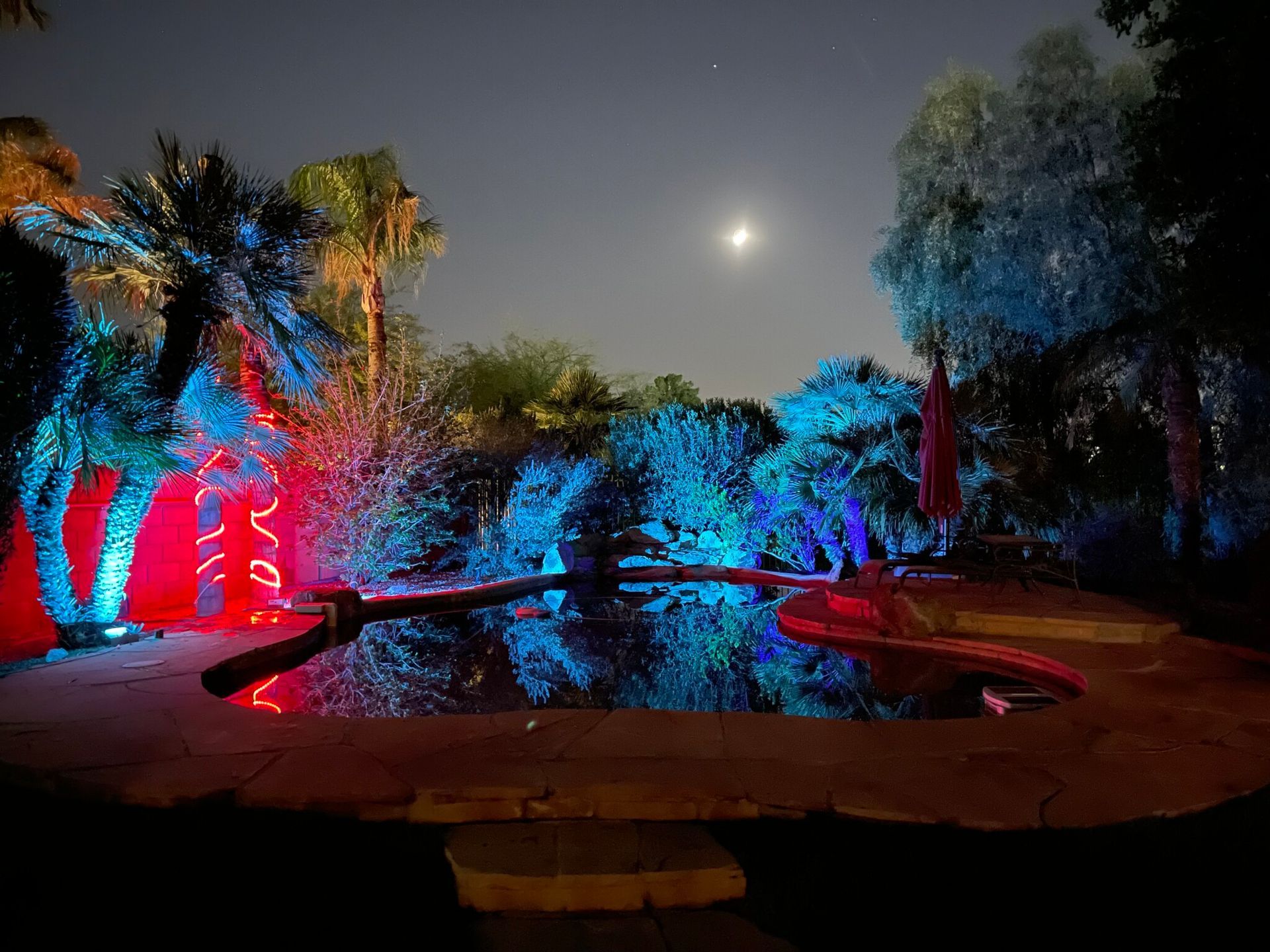 A swimming pool is lit up with blue and red lights at night.