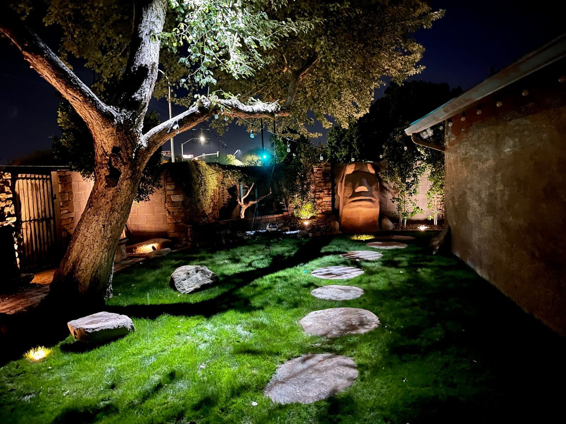 A backyard with a tree and stepping stones lit up at night