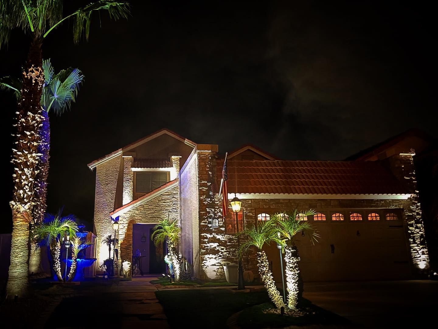 A house is lit up at night with palm trees in front of it