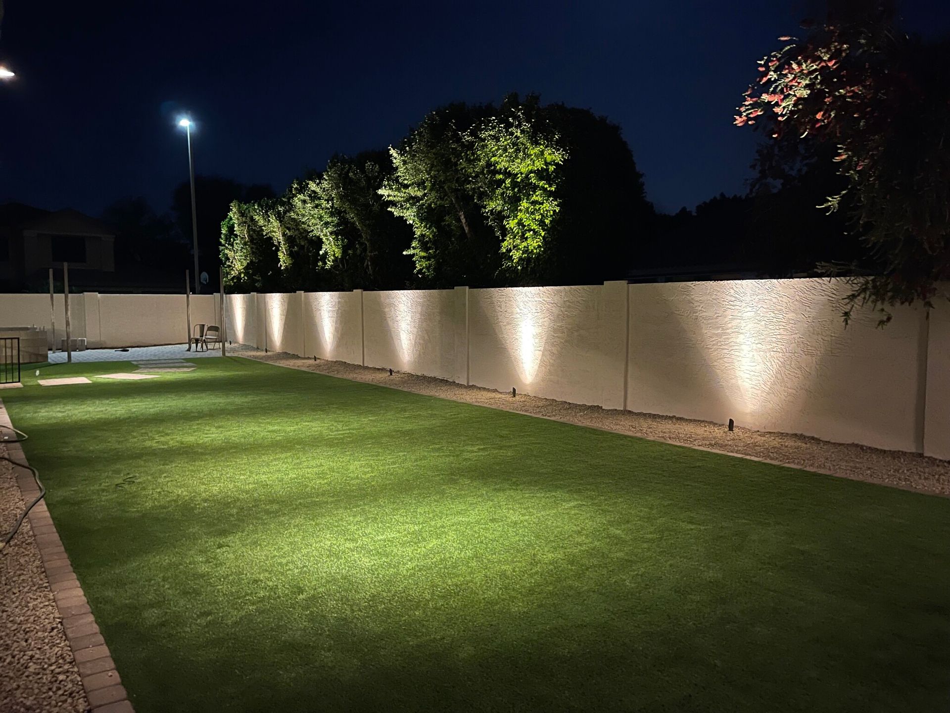 A fence is lit up at night in a backyard.