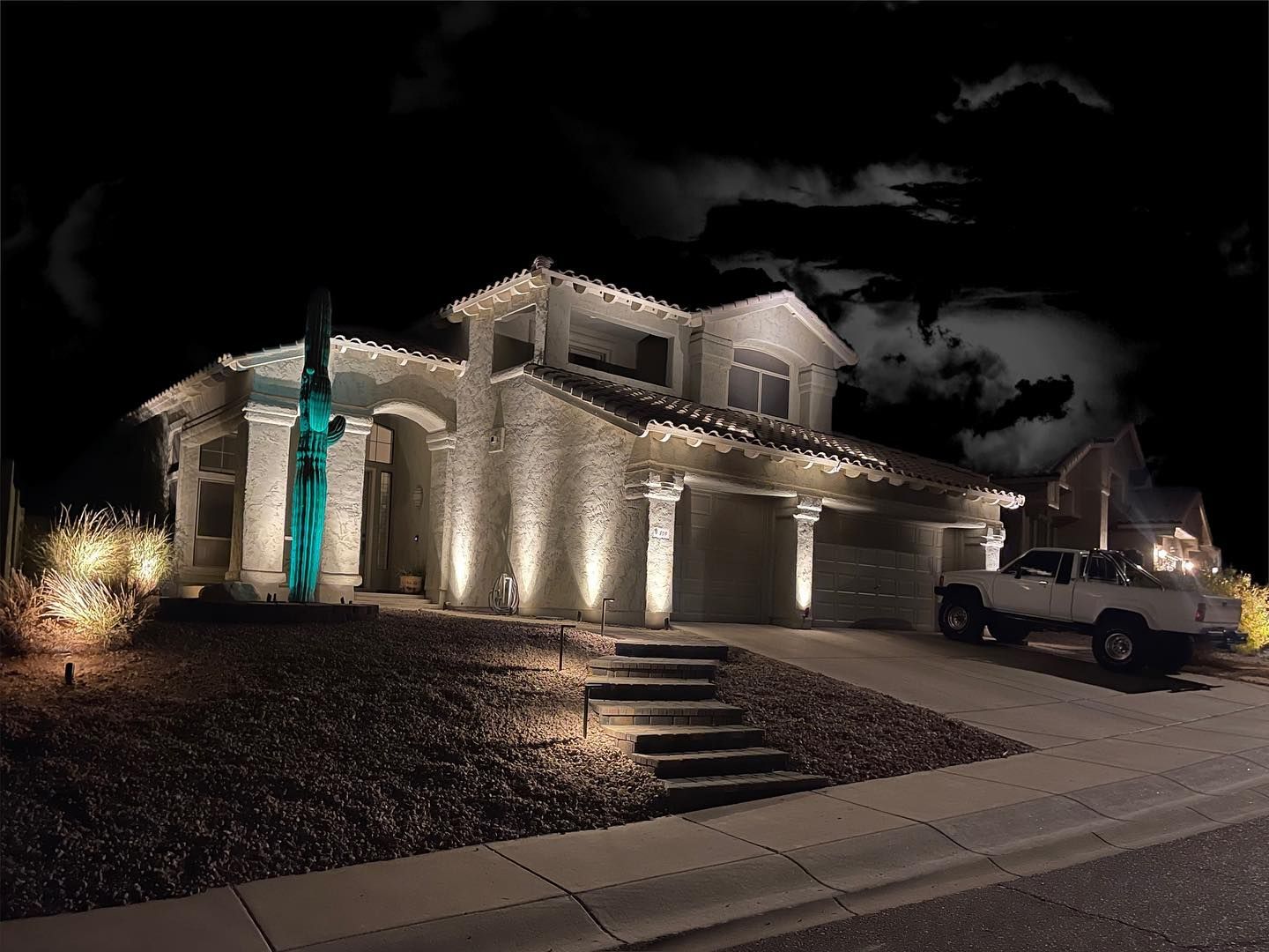 A white truck is parked in front of a house at night.
