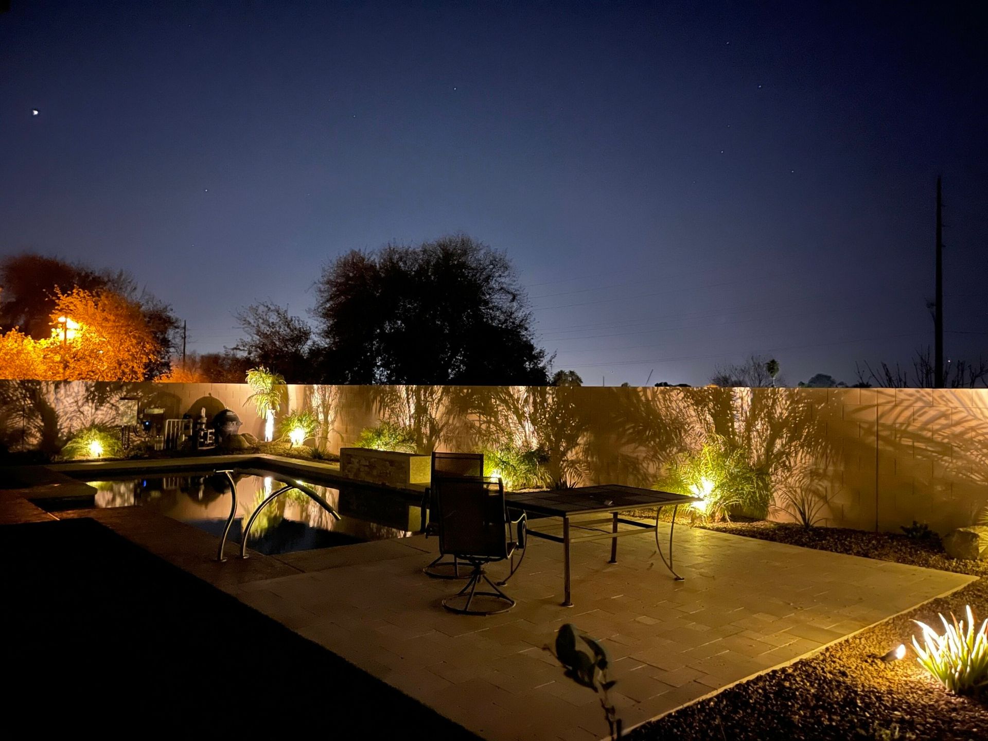 A backyard with a pool and chairs at night