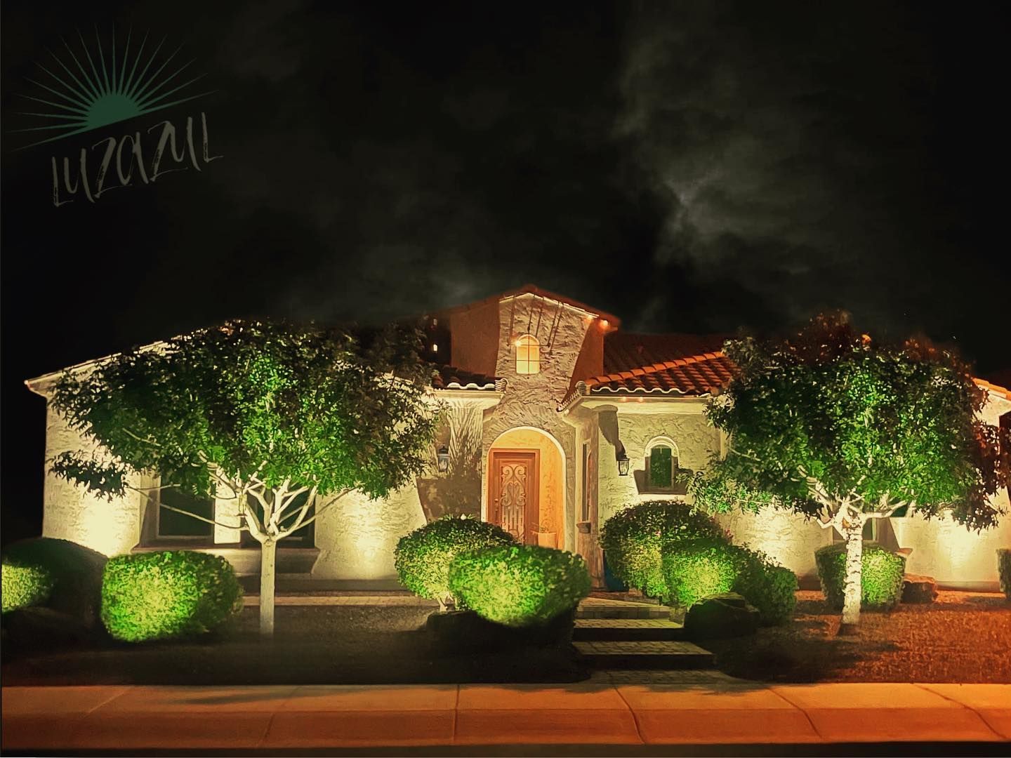 A house is lit up at night with trees and bushes in front of it