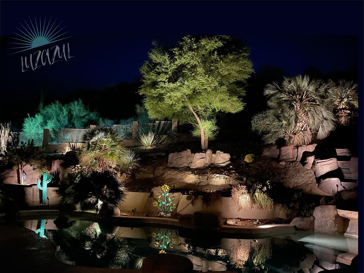 A swimming pool is lit up at night with trees and rocks in the background.
