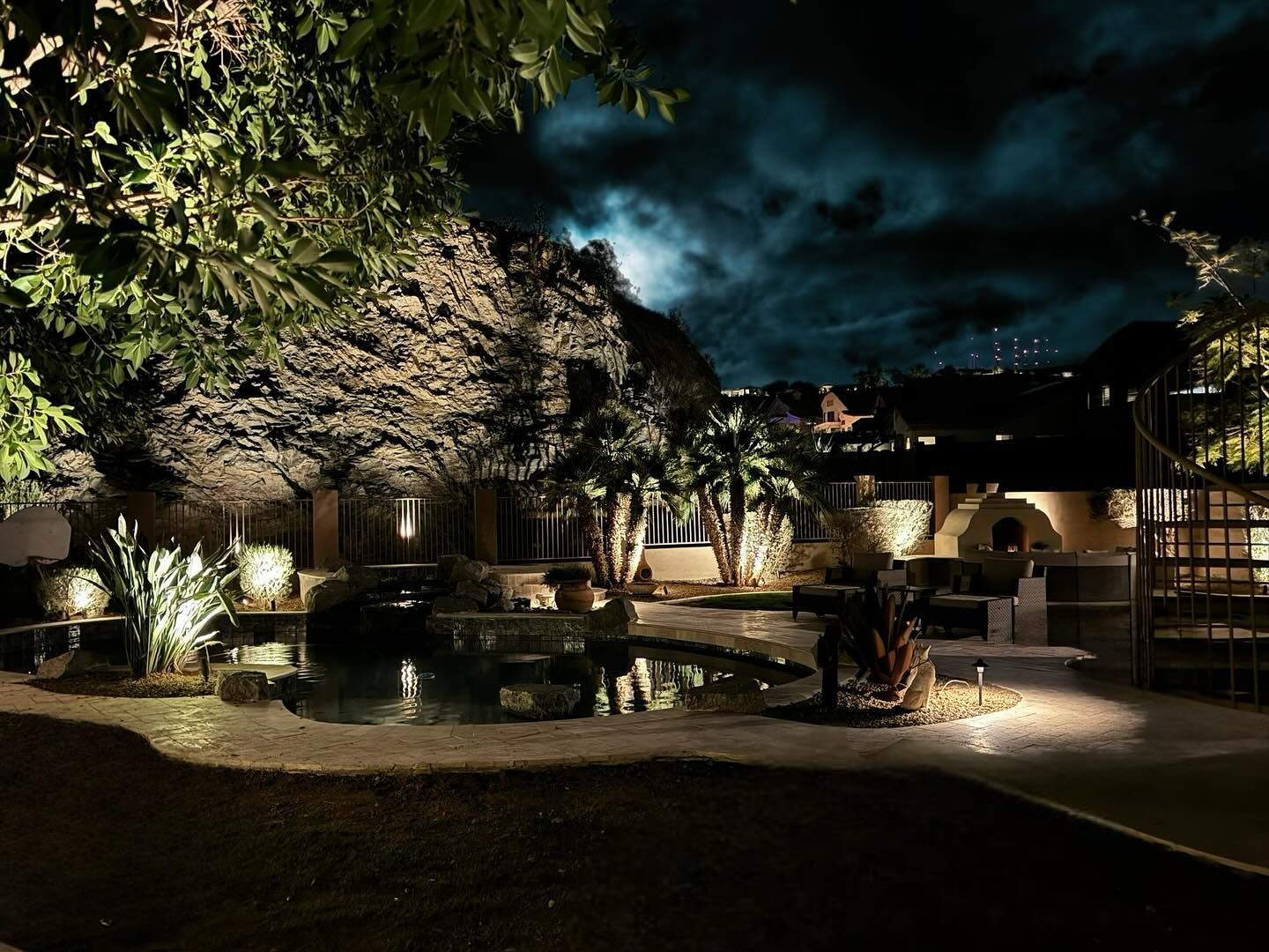 A swimming pool is lit up at night and surrounded by trees.