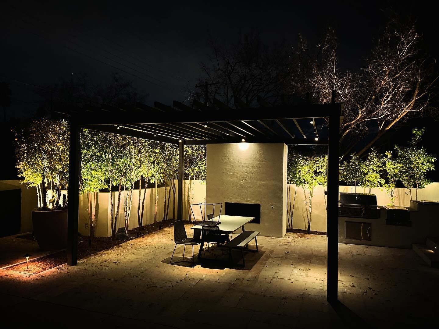 A patio with a table and chairs under a pergola at night