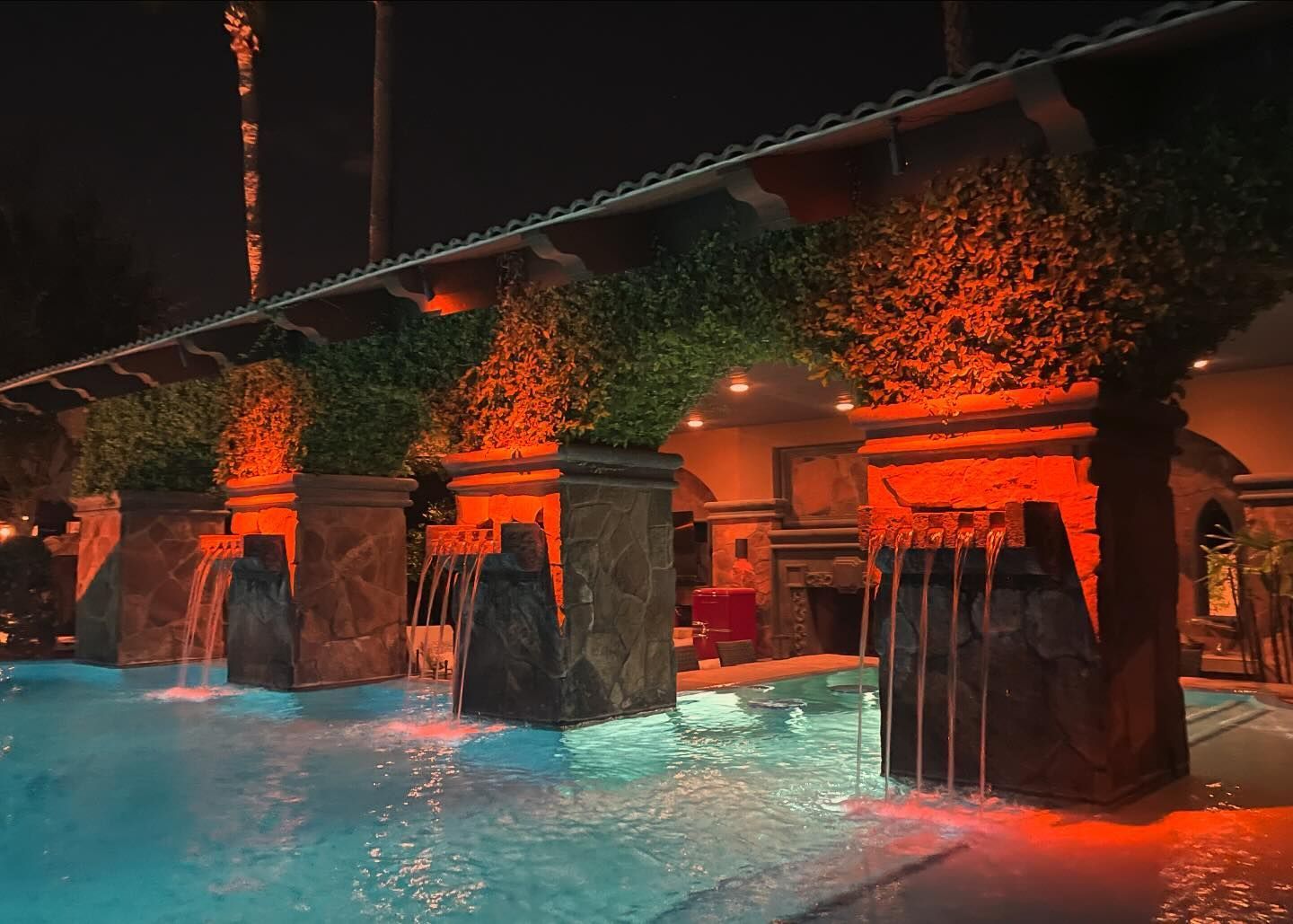 A large swimming pool with a waterfall in the middle of it at night.