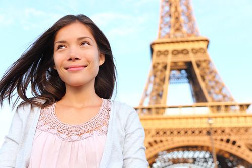 Woman smiling in front of the Eiffel Tower, wearing a pink top and gray cardigan.