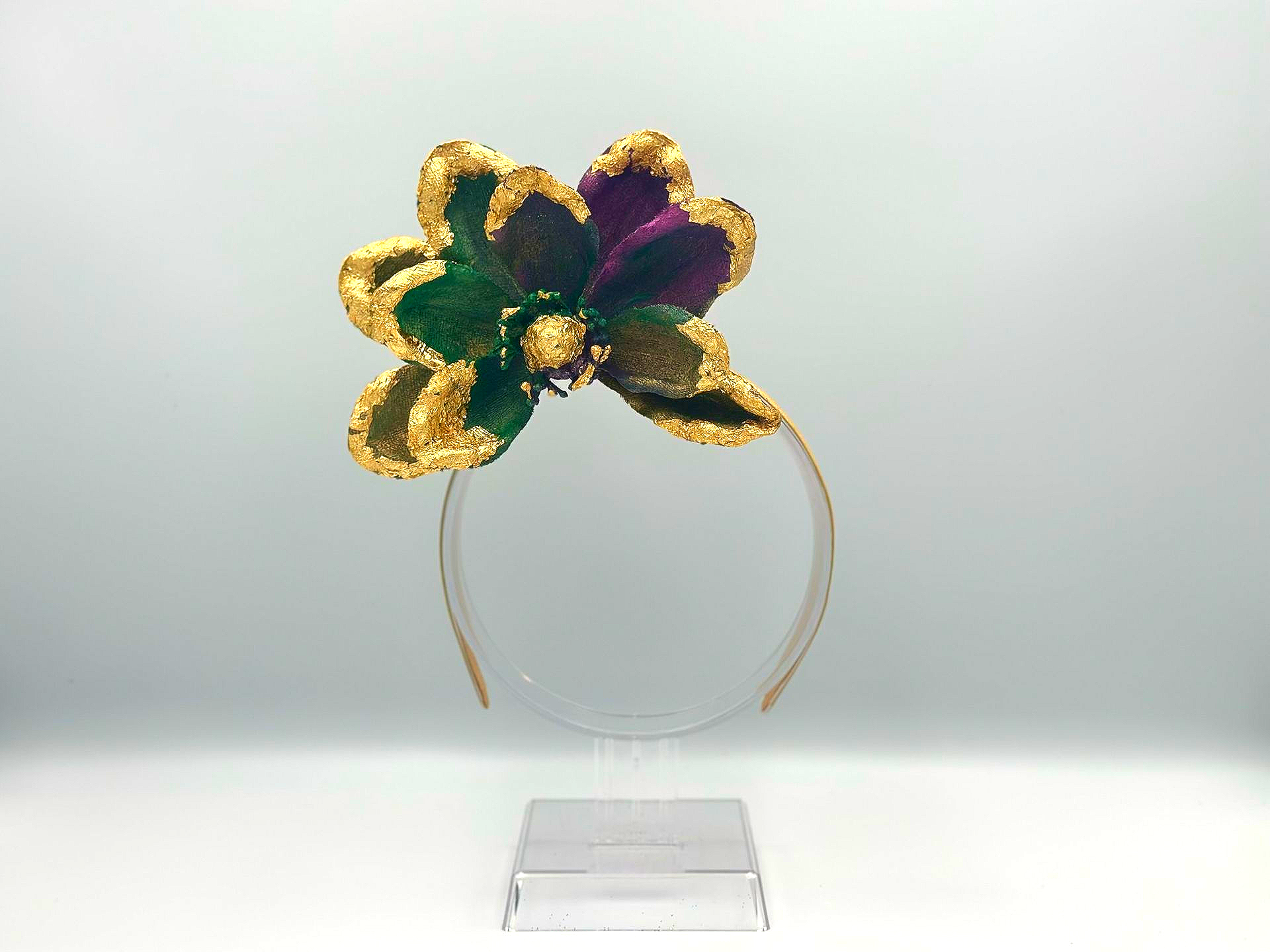 A gold, green, and purple sequined flower headband on a clear stand.